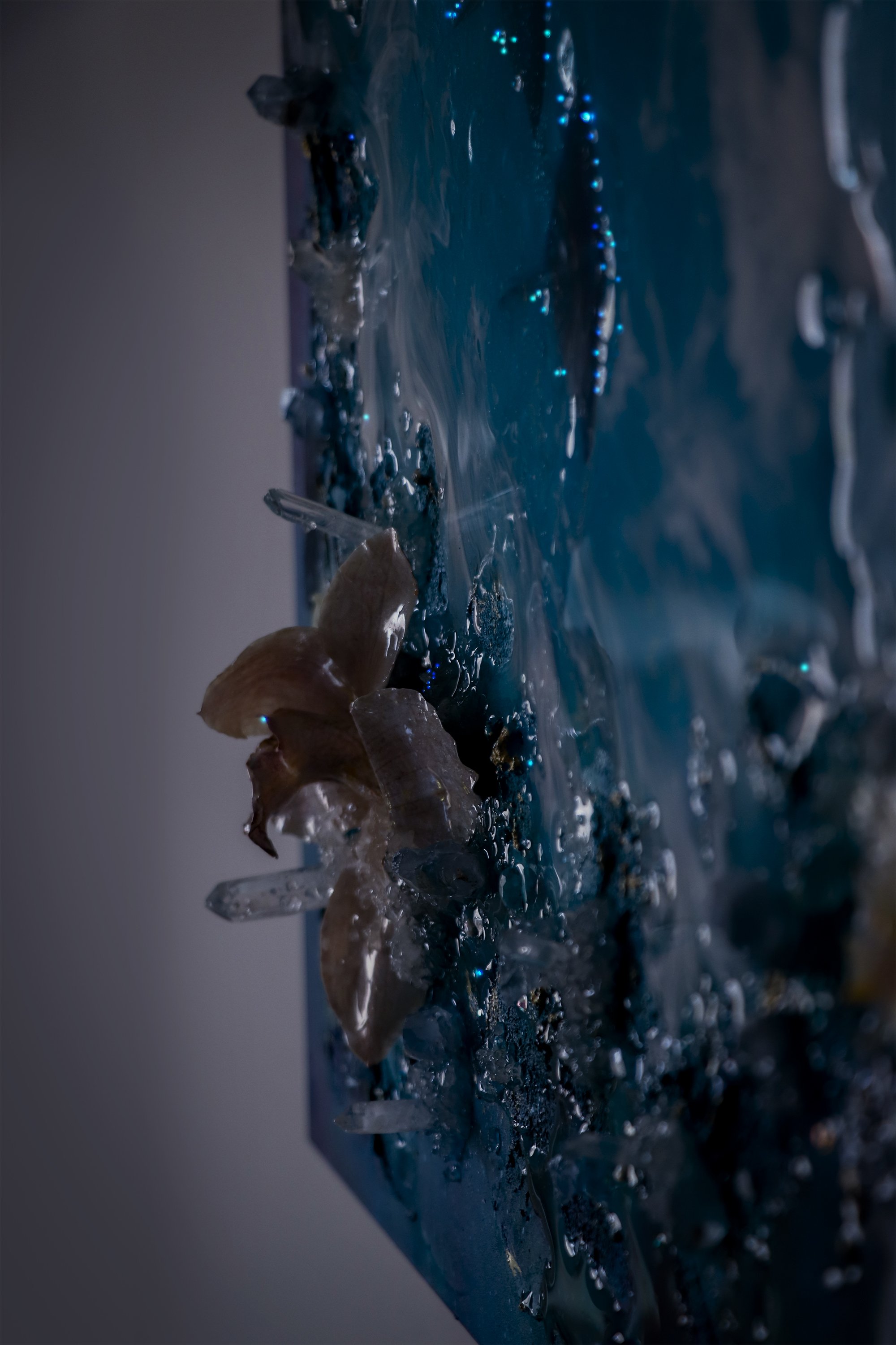 CLose up detail photo of blue abstract space art, darker photo to show details of glowing fiber optic lights, quartz crystals and orchid botanical on textured art