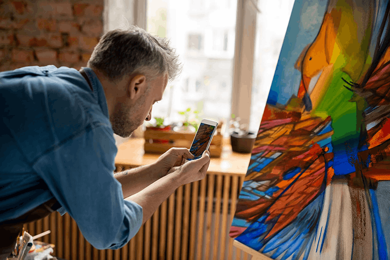Man taking a photo of an abstract colorful painting in an art studio.