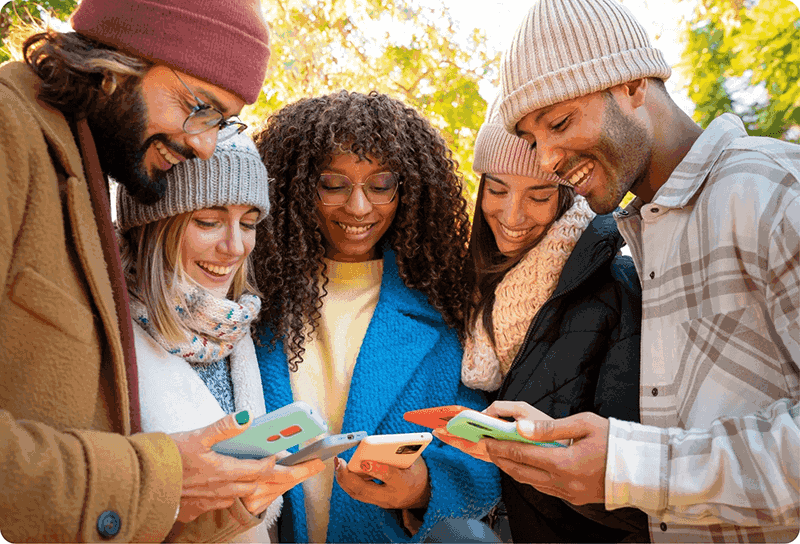 A diverse group of friends outdoors looking at their smartphones and smiling.