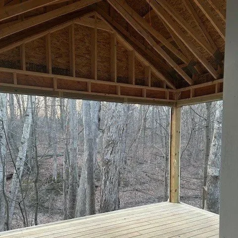 View of a wooden deck under construction with exposed framing, overlooking a wooded area with leafless trees.