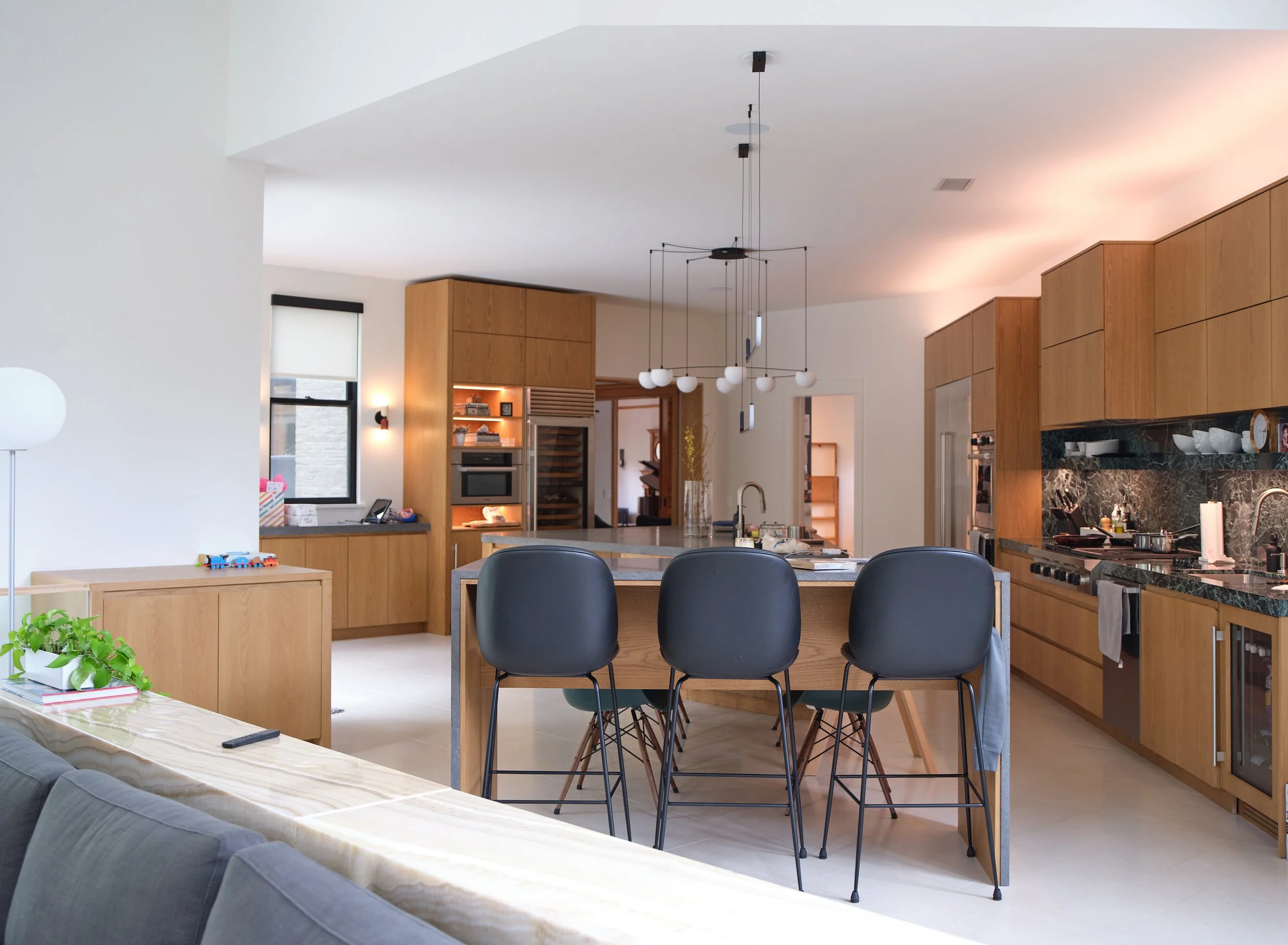 Modern kitchen and dining area with black chairs, wooden cabinets, hanging light fixtures, and kitchen appliances.