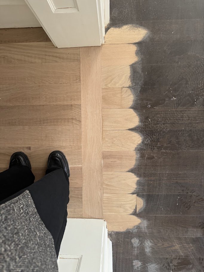 Transitioning hardwood floors from a light natural wood finish to a darker stain near a door.