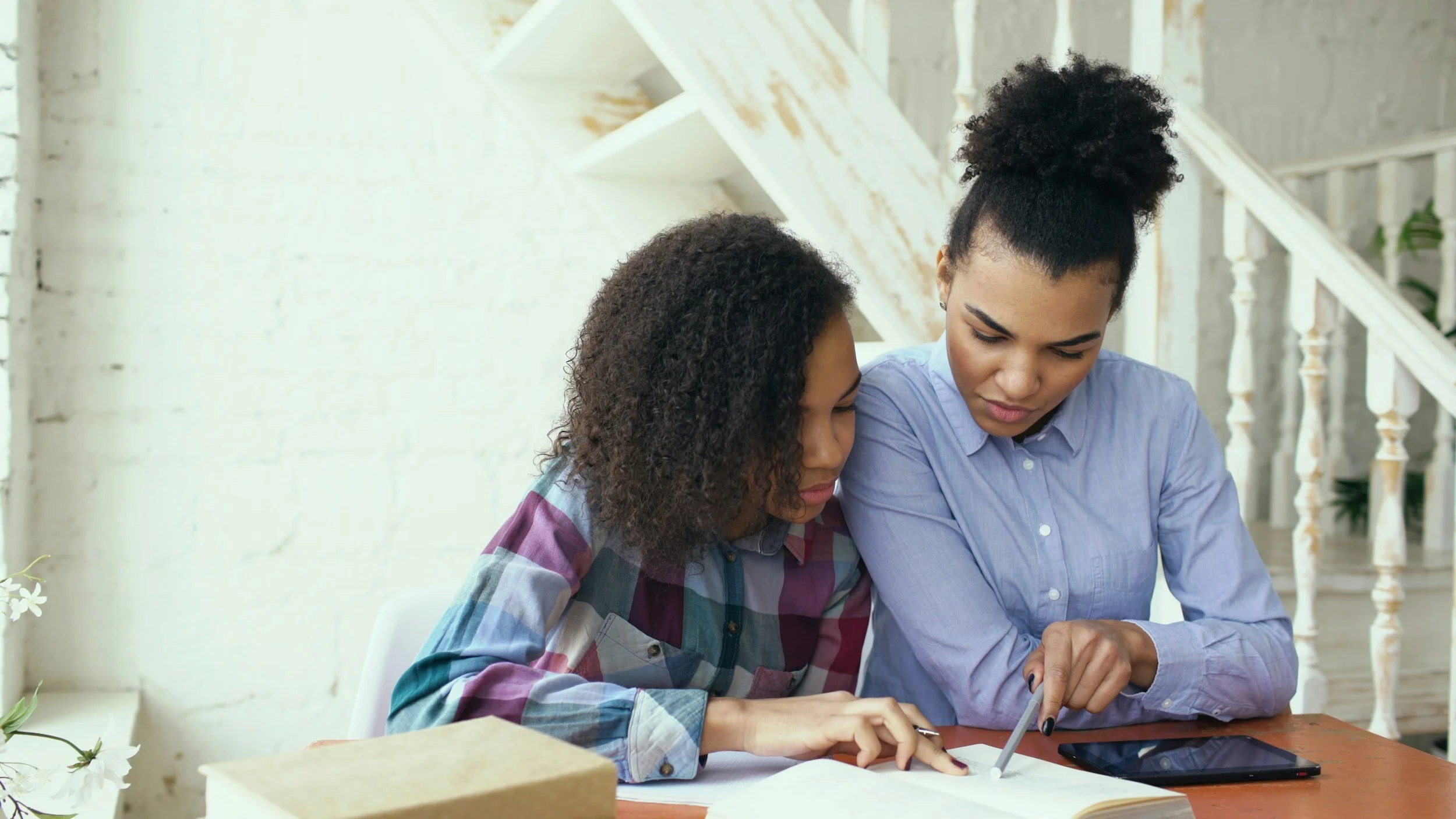 A woman helping a young girl with schoolwork at a table, representing family-centered child and adolescent psychiatric care by Linda Perry PMHNP-BC in Caldwell and Saddle River NJ