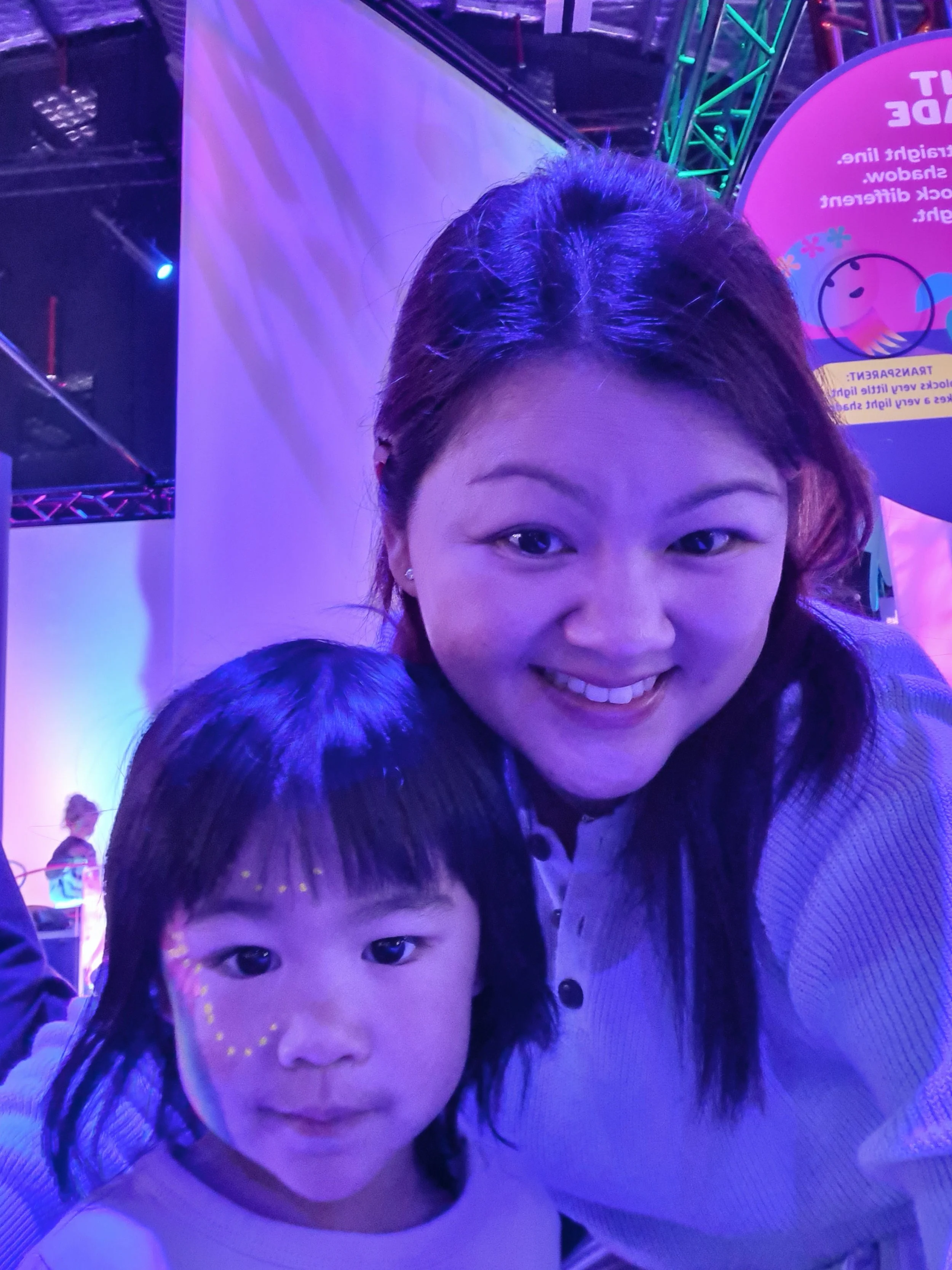 A woman and a child taking a selfie together at an indoor event with colorful lighting.
