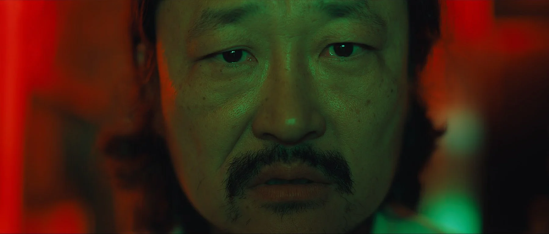 Pedigree short film still — Kai Wen Hu - Close-up of a Samuel's face with intense expression, surrounded by mysterious green and red lighting.
