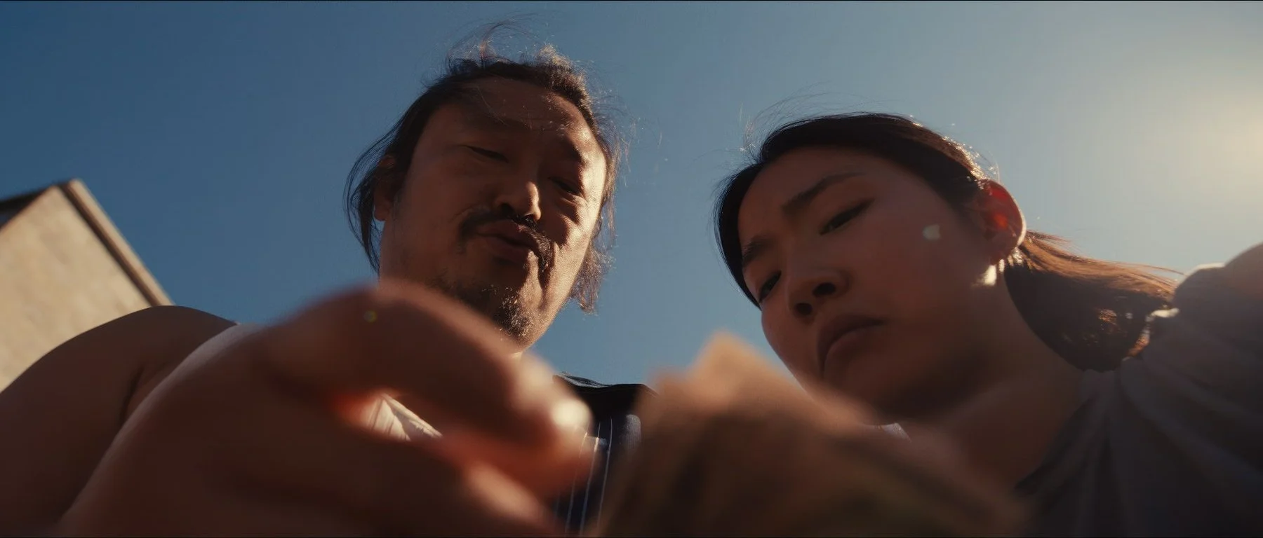 Pedigree short film still — Kai Wen Hu - Samuel and Squid count money against a blue sky.