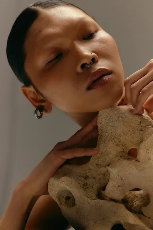 An Asian woman wear a black tank top, holding a shell against her ear, with her eyes closed