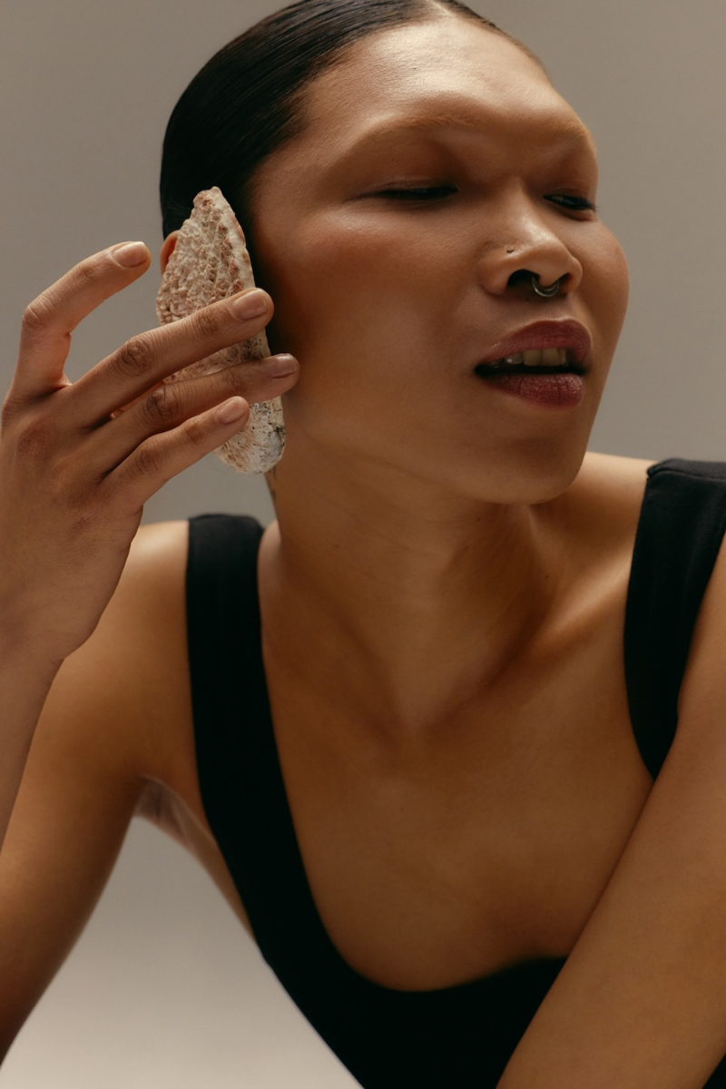 An asian woman wearing a black tank top, holding a white rock to her ear