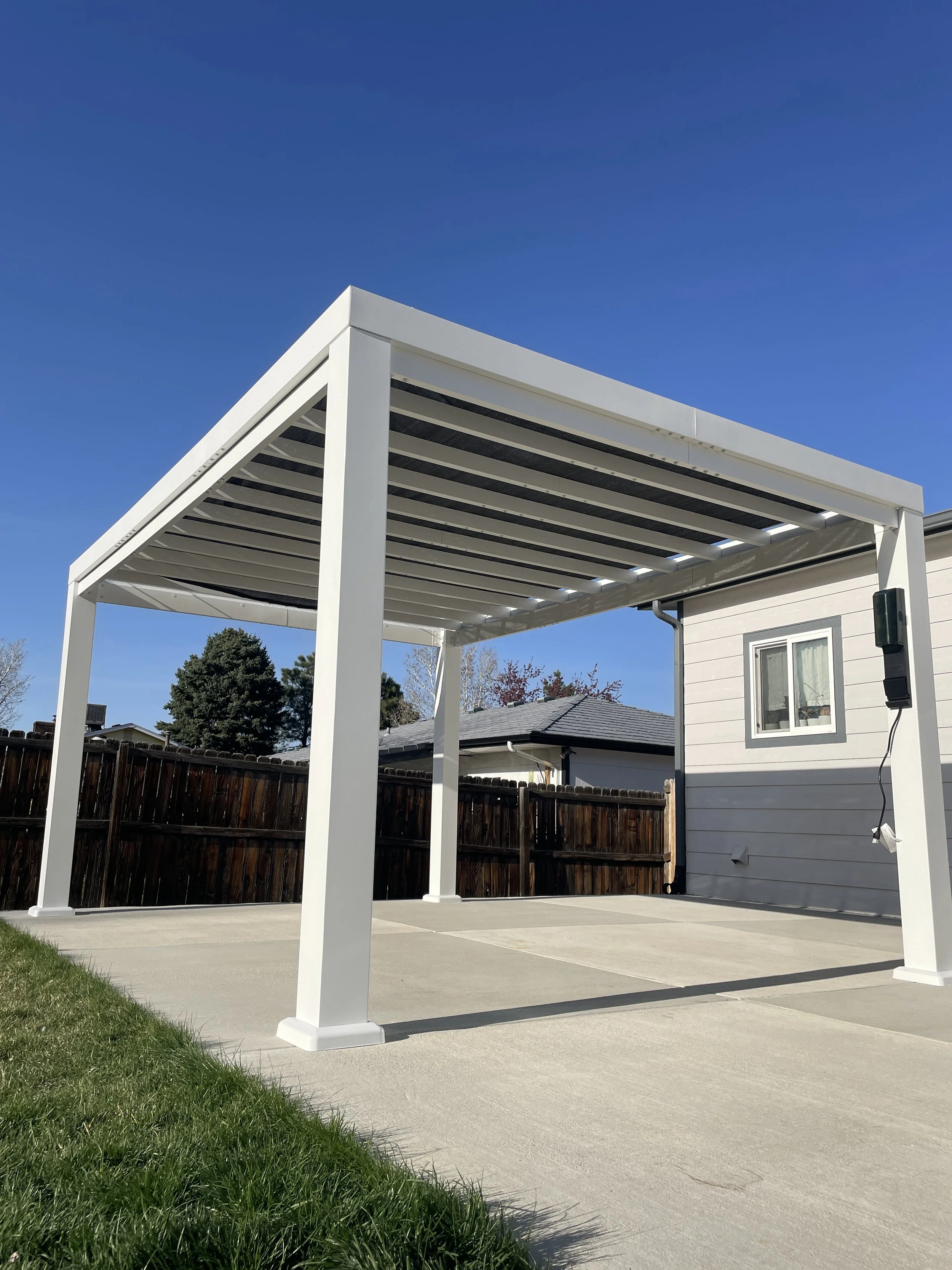A backyard patio with a white pergola, concrete flooring, and a wooden fence in the background.