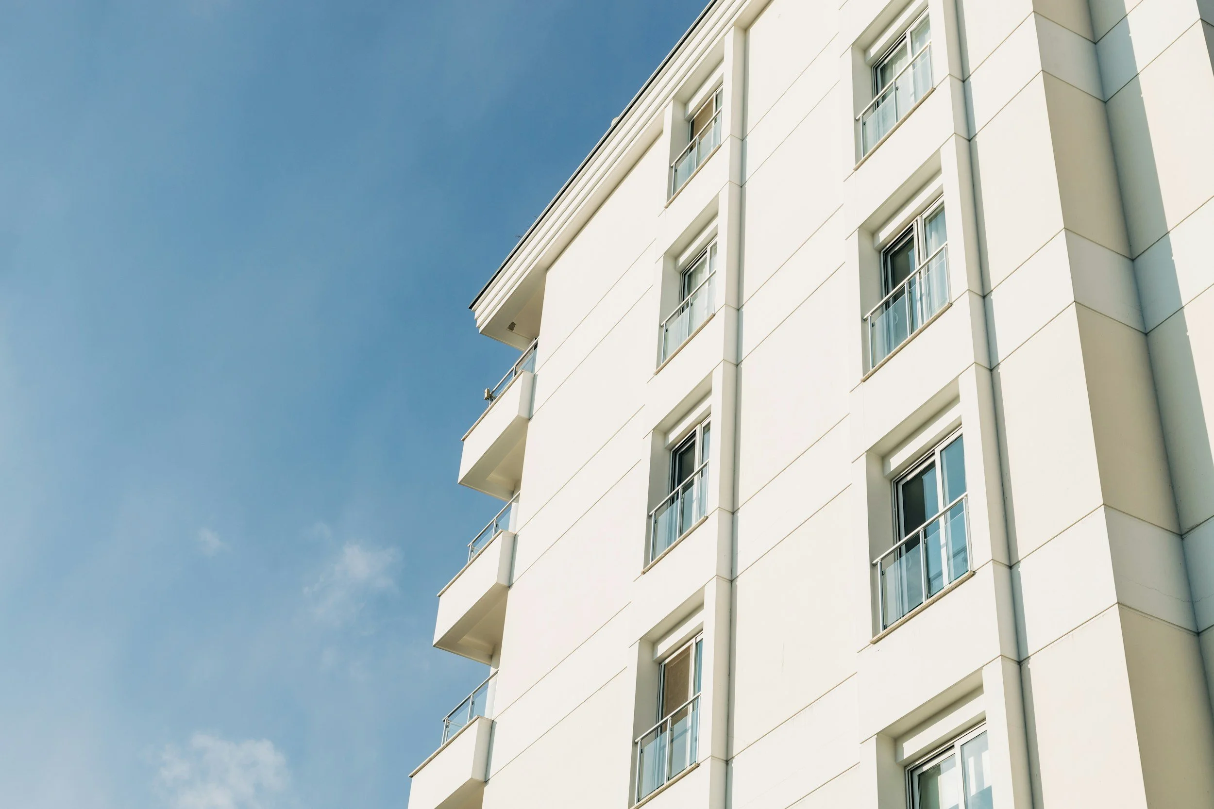 Close-up of a modern white apartment building with small balconies and windows under a clear blue sky.