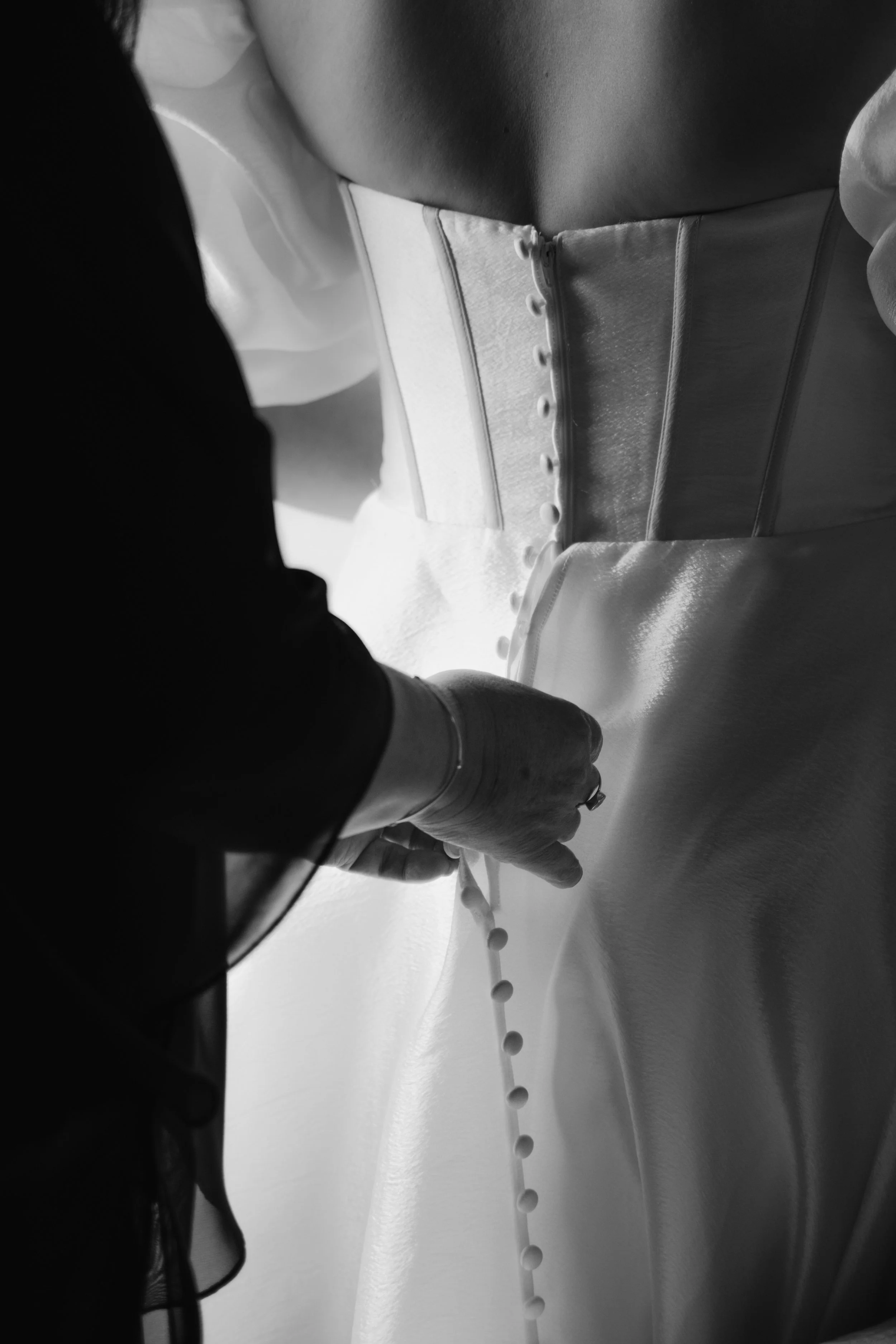 Close-up of a person buttoning the back of a wedding dress.