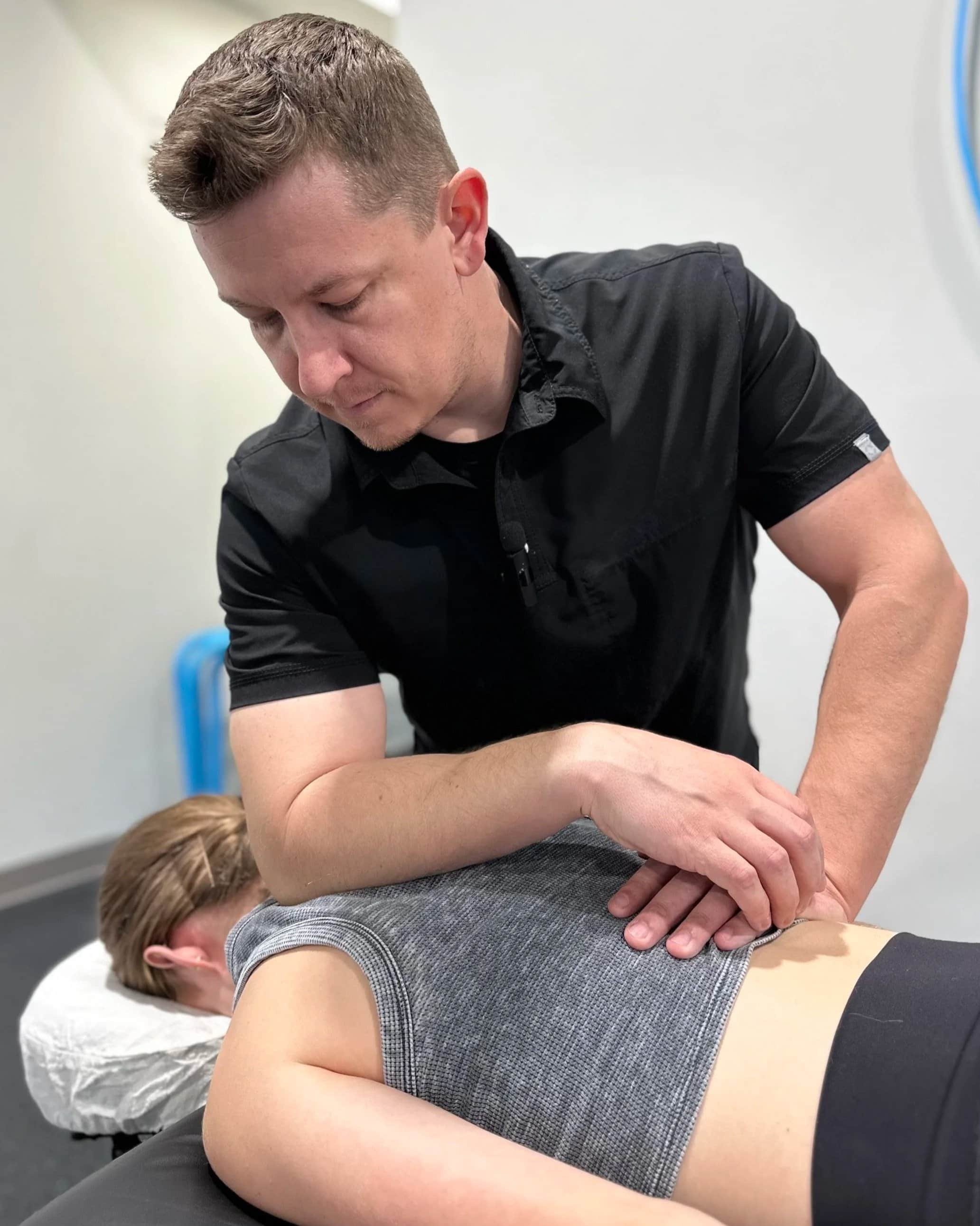 A male chiropractor is performing an adjustment on a female patient's back in a clinical setting.