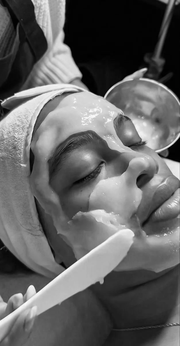 Person receiving a facial mask treatment, with gel-like substance applied to their face, and a cosmetic spatula used for application.