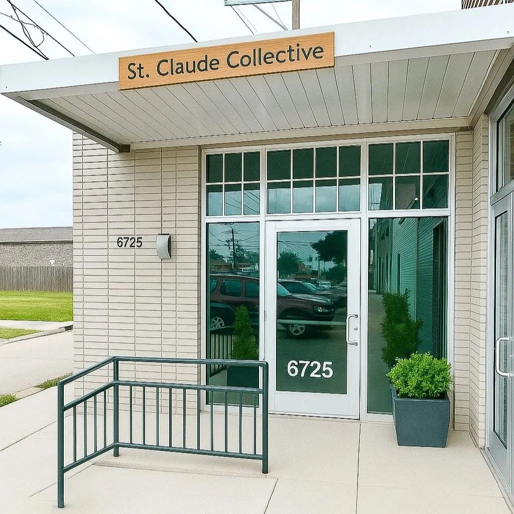 The entrance of a building labeled "St. Claude Collective" with the street number 6725. There are large windows and a potted plant outside. A small metal railing is in front of the entrance.