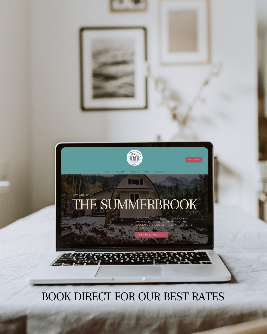 Laptop displaying the website for The Summerbrook, a lakeside cabin rental, on a bed in a cozy room with framed pictures and a plant in the background.