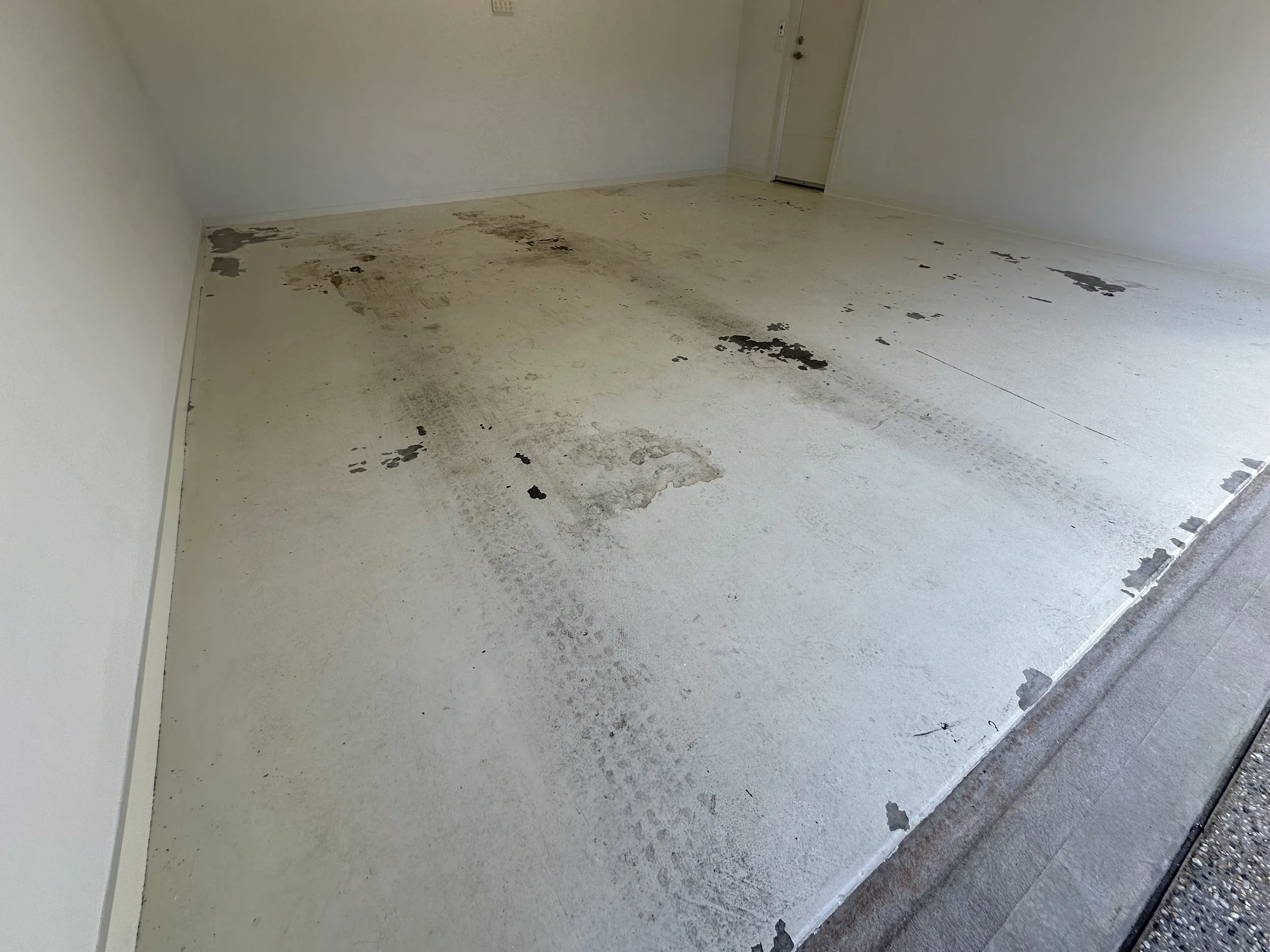 Dirty, stained garage floor with patches of peeling paint near the doorway.