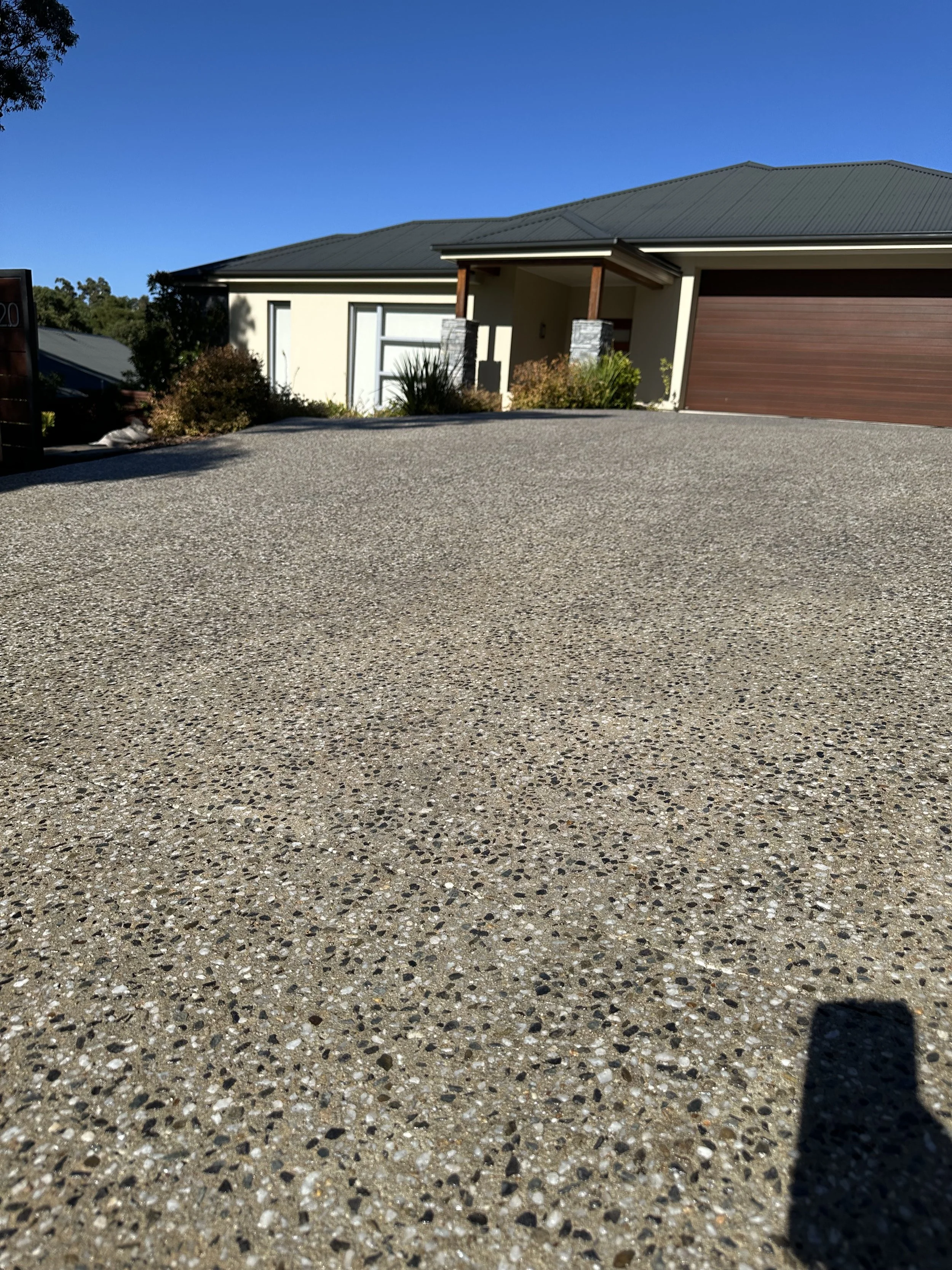 View of a modern house with a gravel driveway, a garage with a brown door, some bushes, and a clear blue sky.
