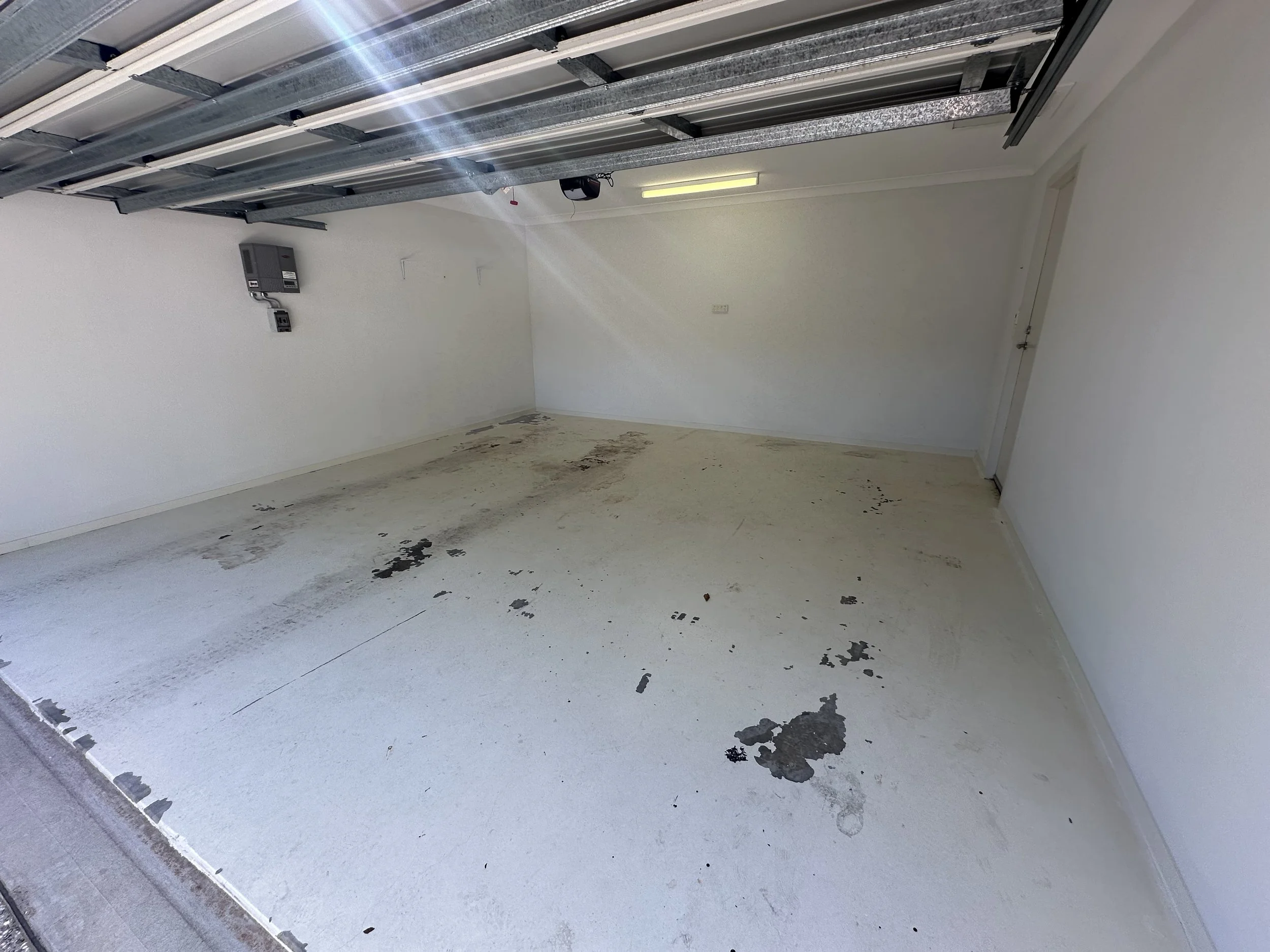 Empty garage with stained and dirty concrete floor, white walls, and a closed garage door.