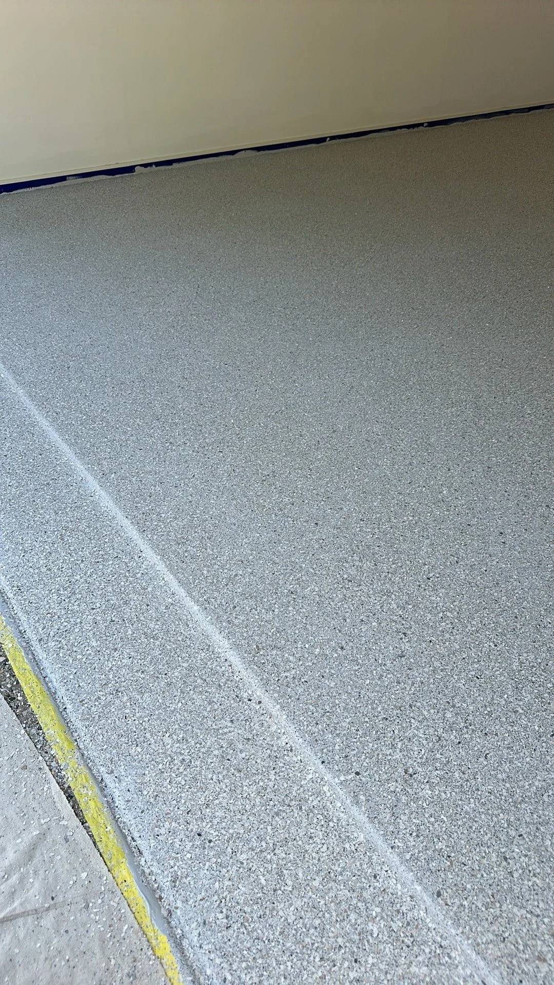 Close-up of a newly poured concrete floor with clean, textured surface and a yellow caution line along the edge.