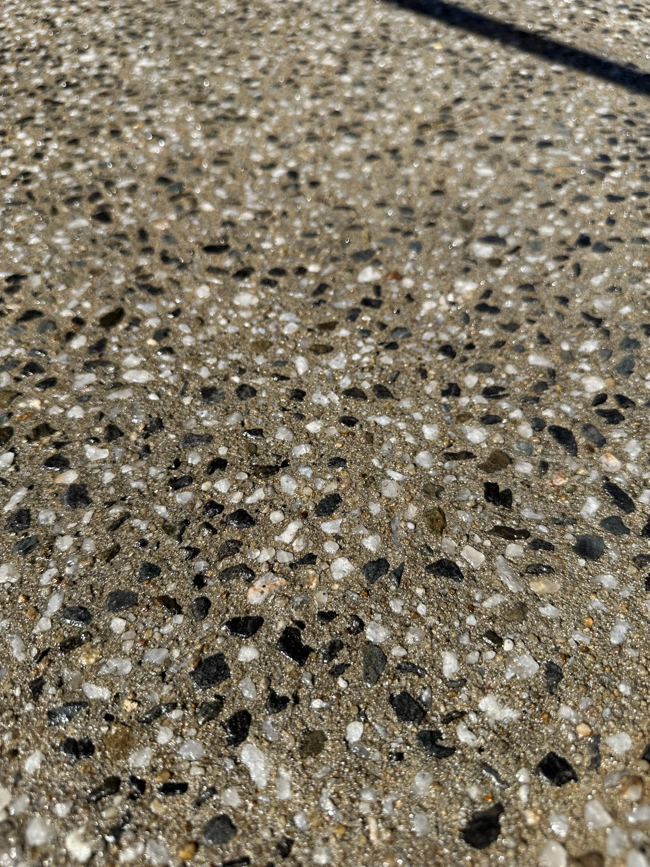 Close-up view of a concrete sidewalk surface with small stones and sand.