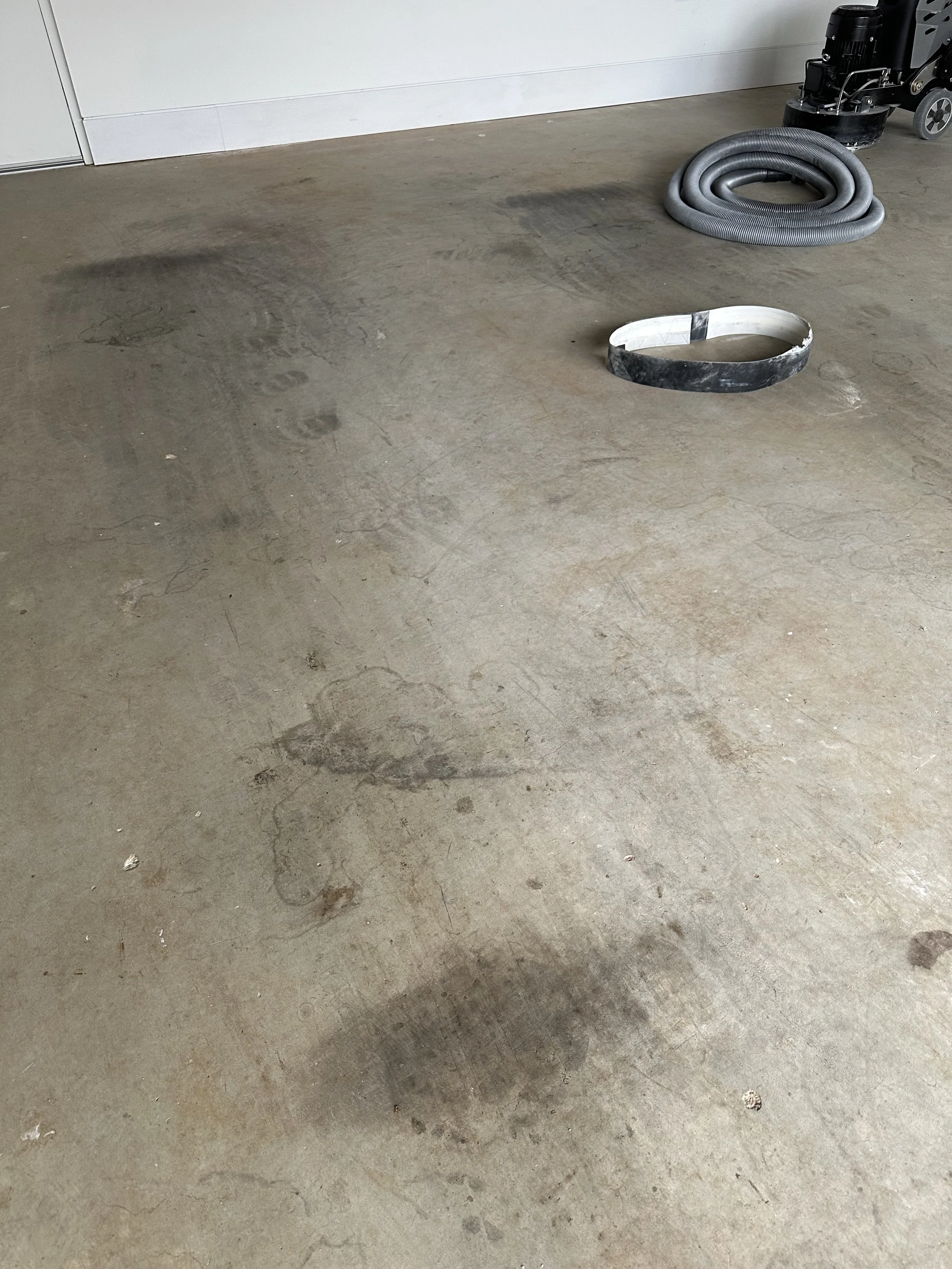 Concrete floor with dirt and oil stains, a coiled vacuum hose, and a circular opening with a black border.