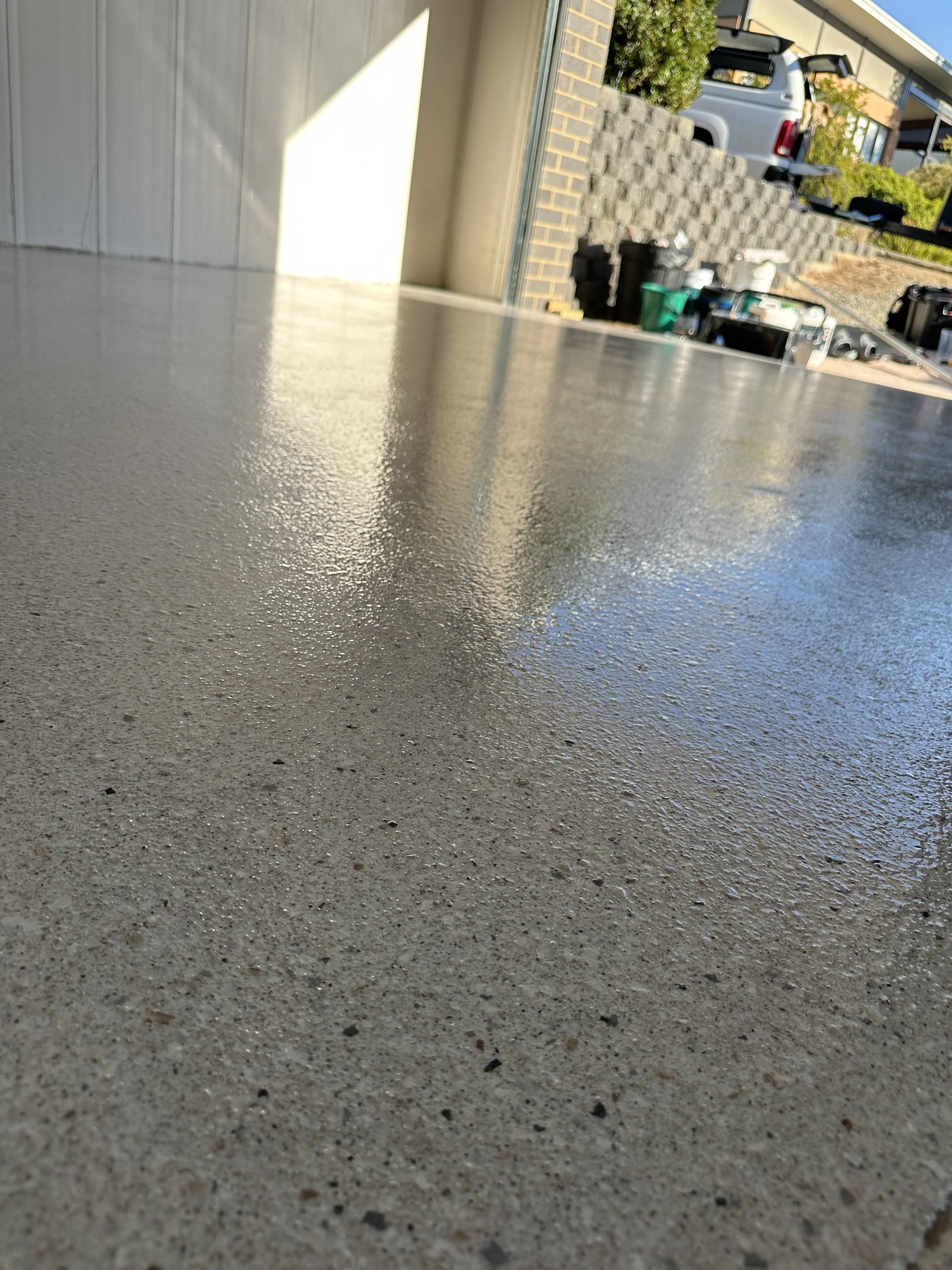 Close-up view of a freshly sealed concrete floor with a reflective surface, during daytime.