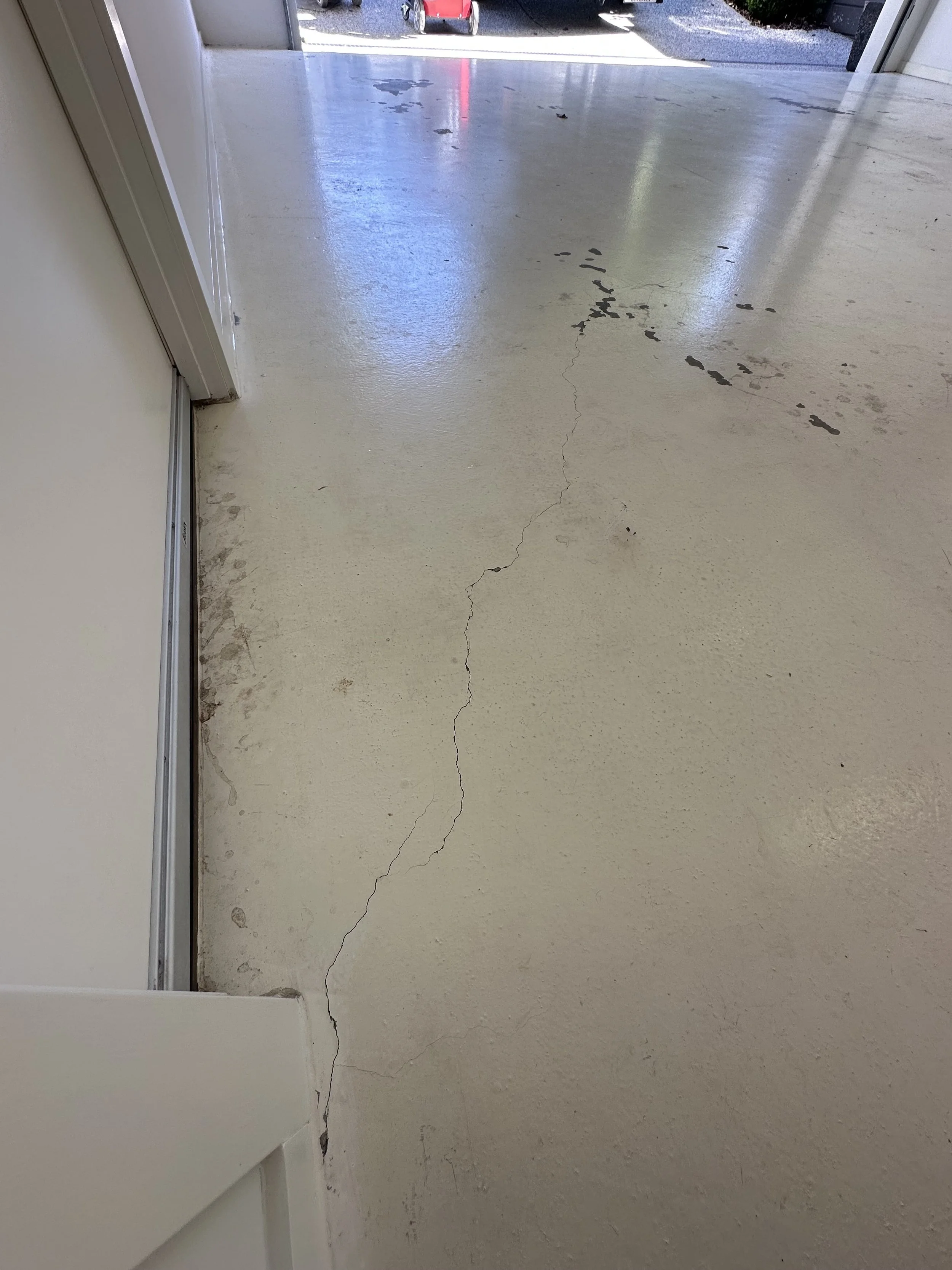 Concrete floor with visible cracks and chipped paint near a door, with outdoor view of parked vehicles.