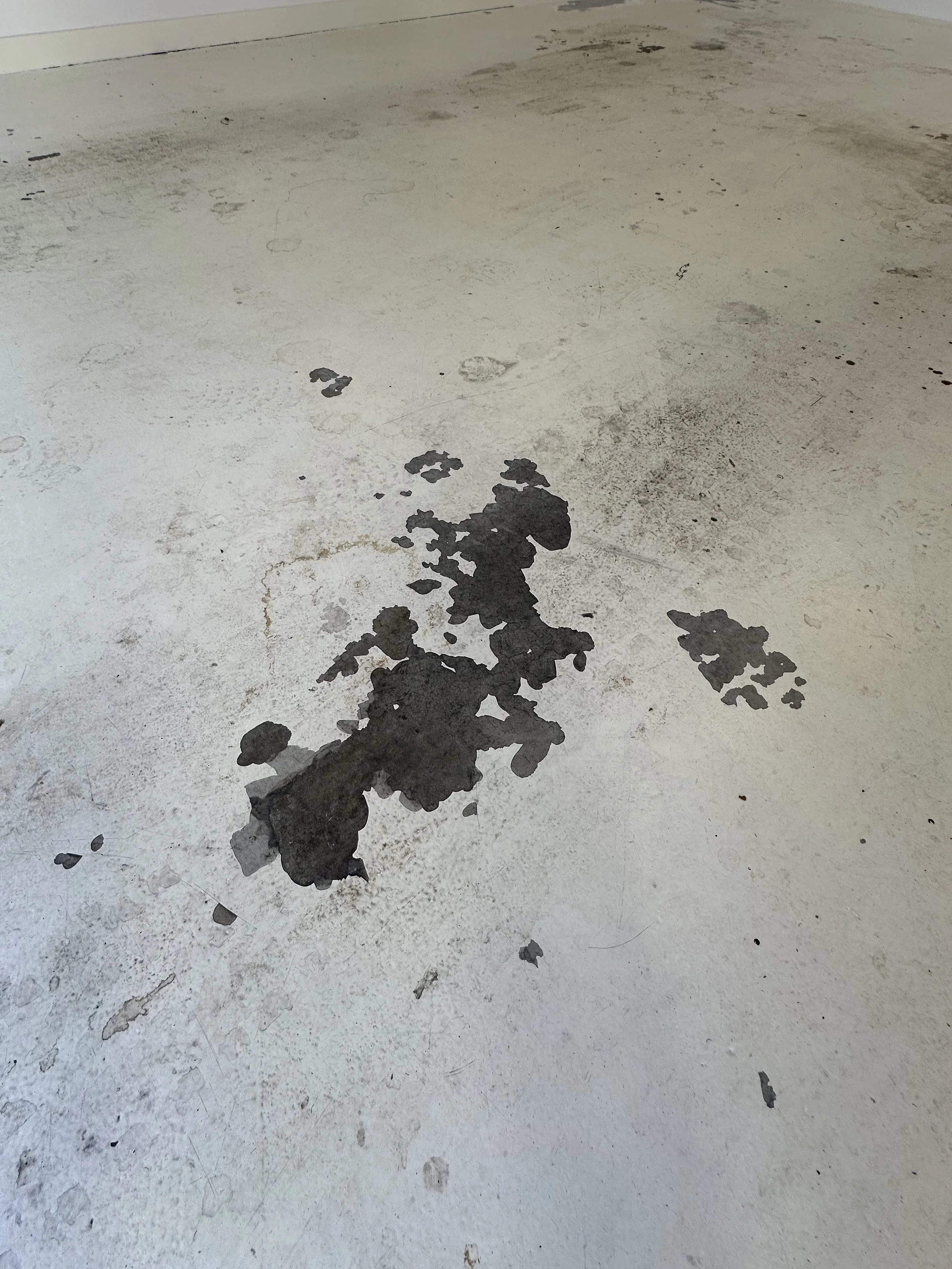 Dirty concrete floor with scattered black paint or oil spills.