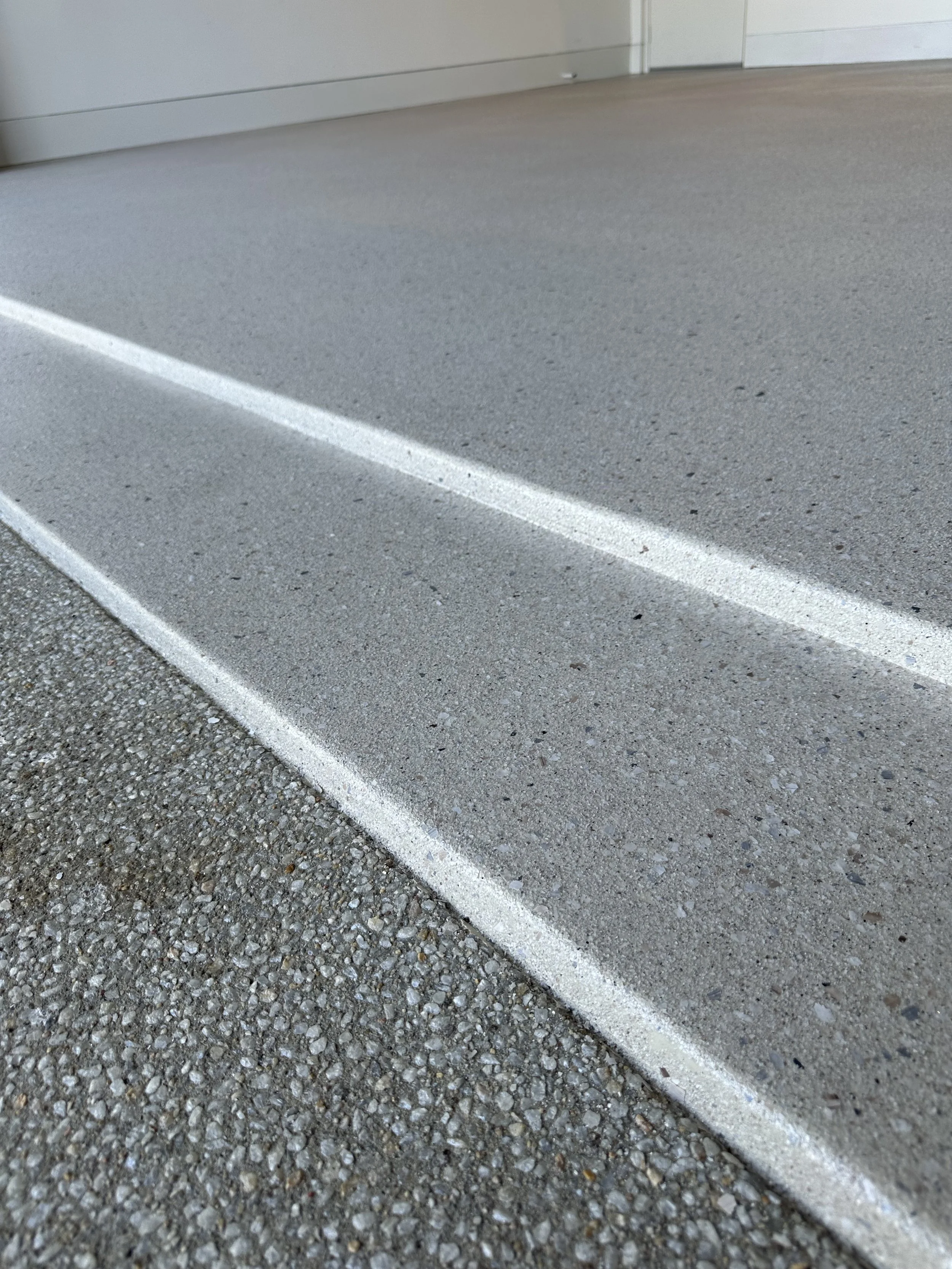 Close-up view of a concrete parking lot with white painted parking lines and a building wall in the background