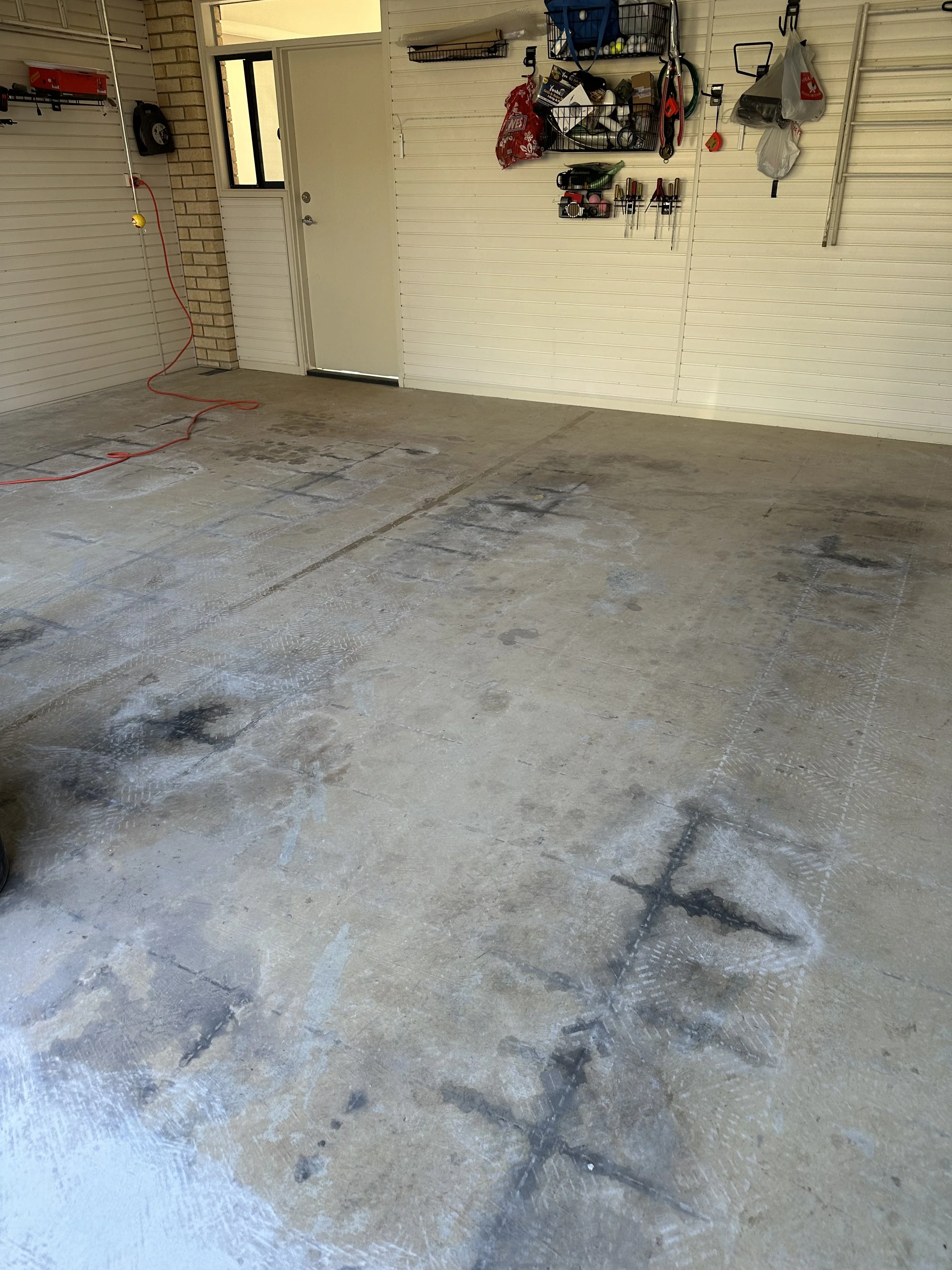 Clean, empty garage with a repaired concrete floor, white slatwall panels, and organized wall storage.