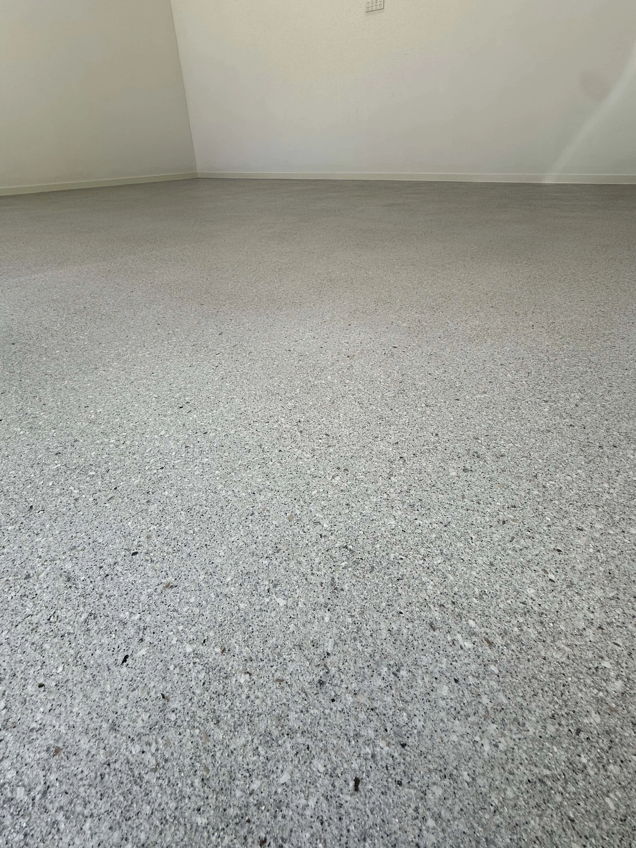 Empty room with light-colored textured floor and plain light-colored walls.