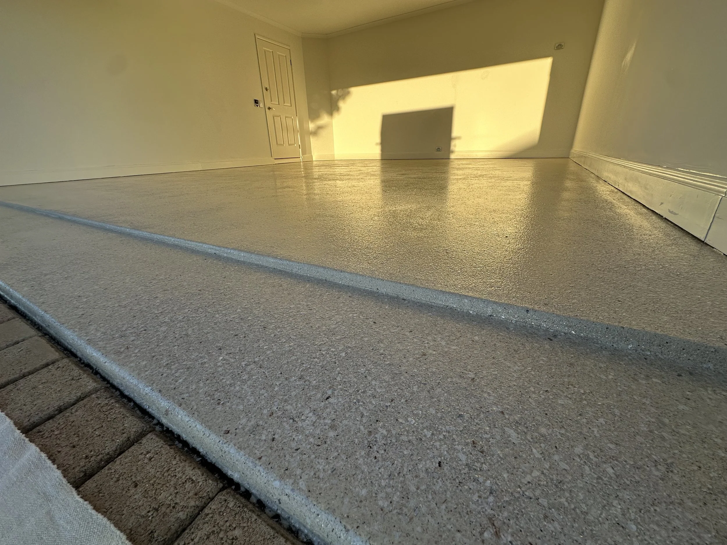 Front porch with newly painted concrete steps and a brick walkway leading to a white door, illuminated by warm sunlight.