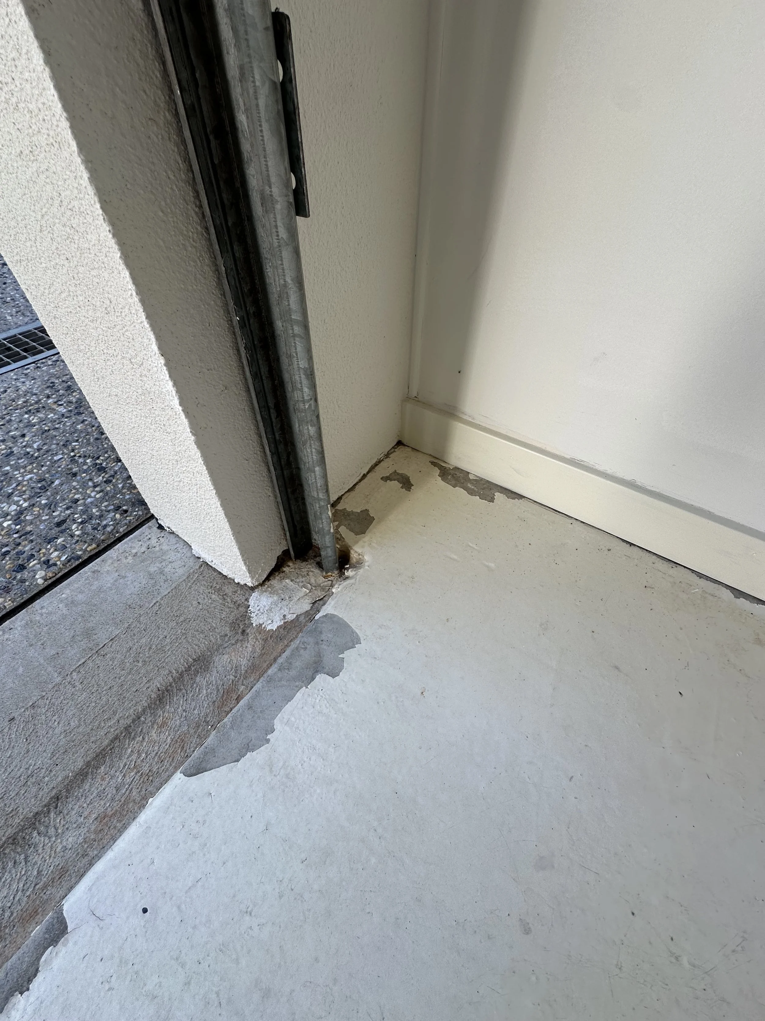 Close-up of a door frame and threshold with some peeling paint and exposed concrete on the floor.