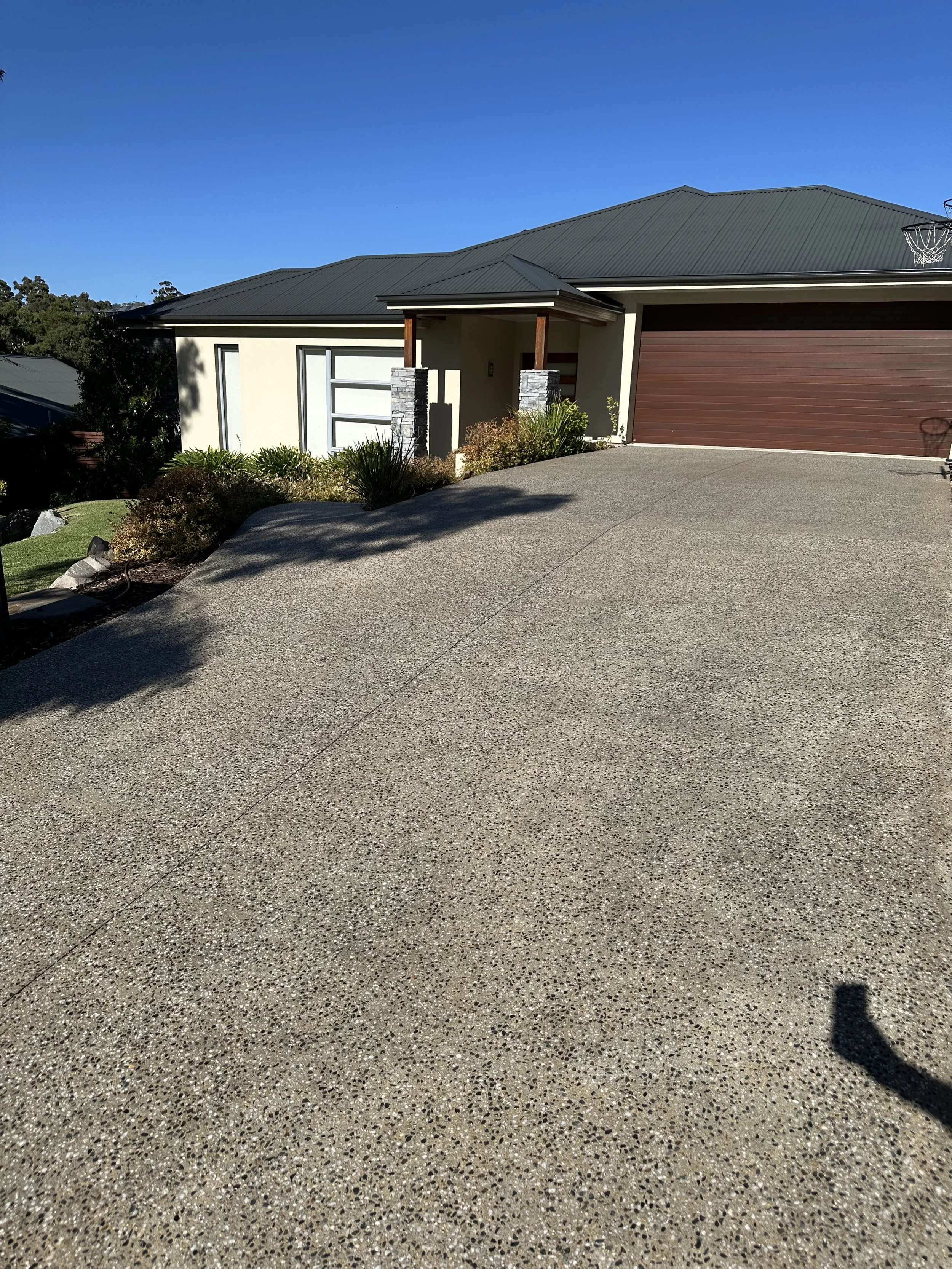 Modern house with a concrete driveway, landscaped yard, and a garage with brown door, under a clear blue sky.