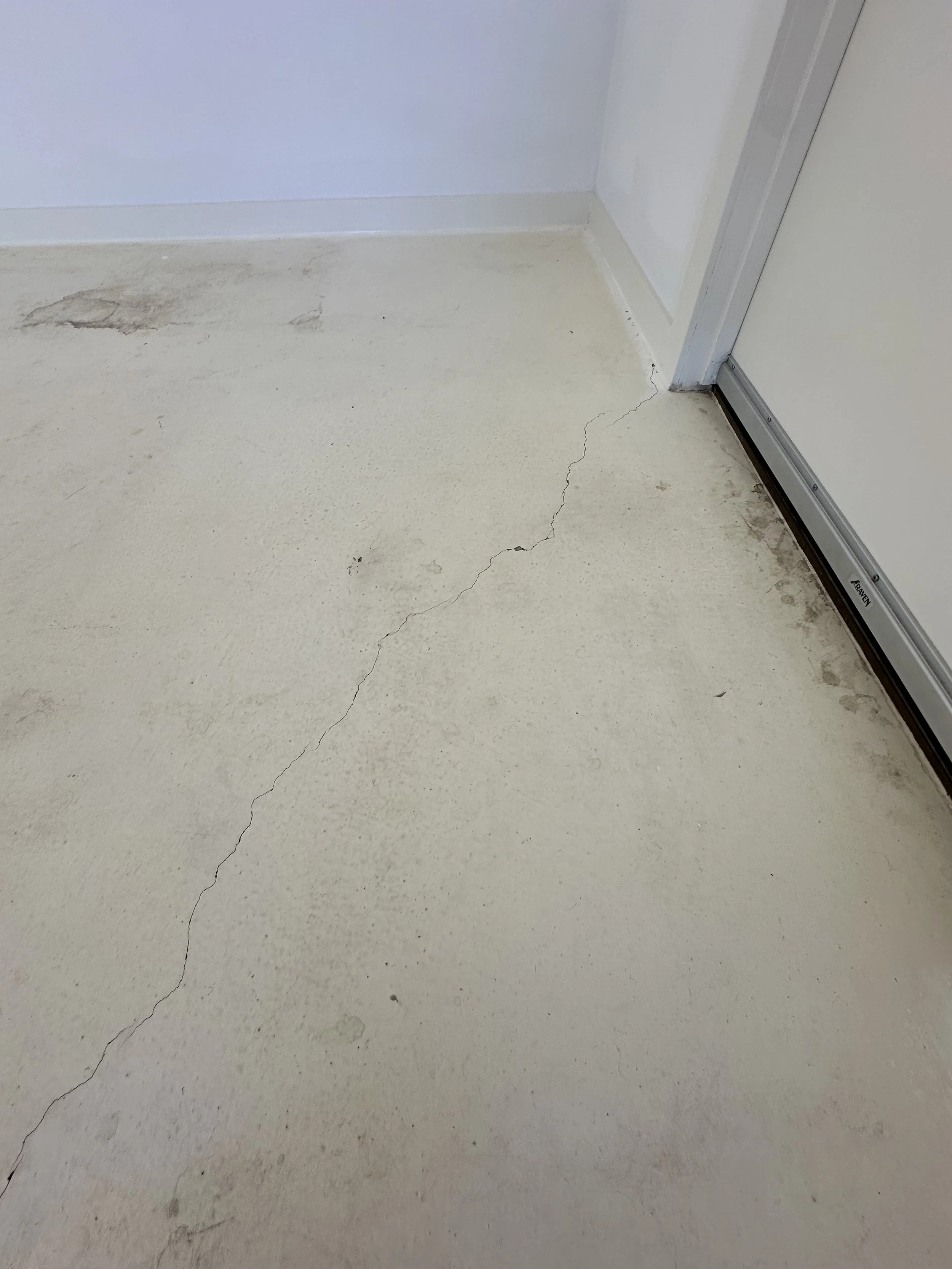 Cracked and stained concrete floor next to a white wall and door.