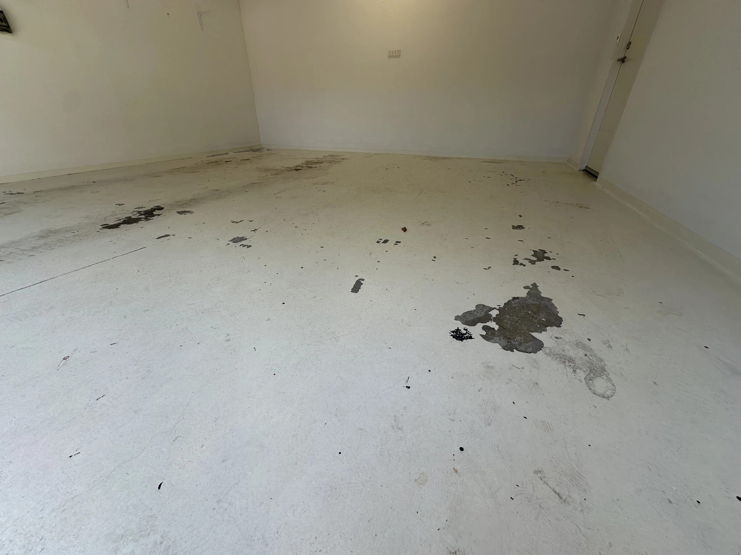 Empty room with white walls and a white floor, showing dark staining and damage on parts of the floor.