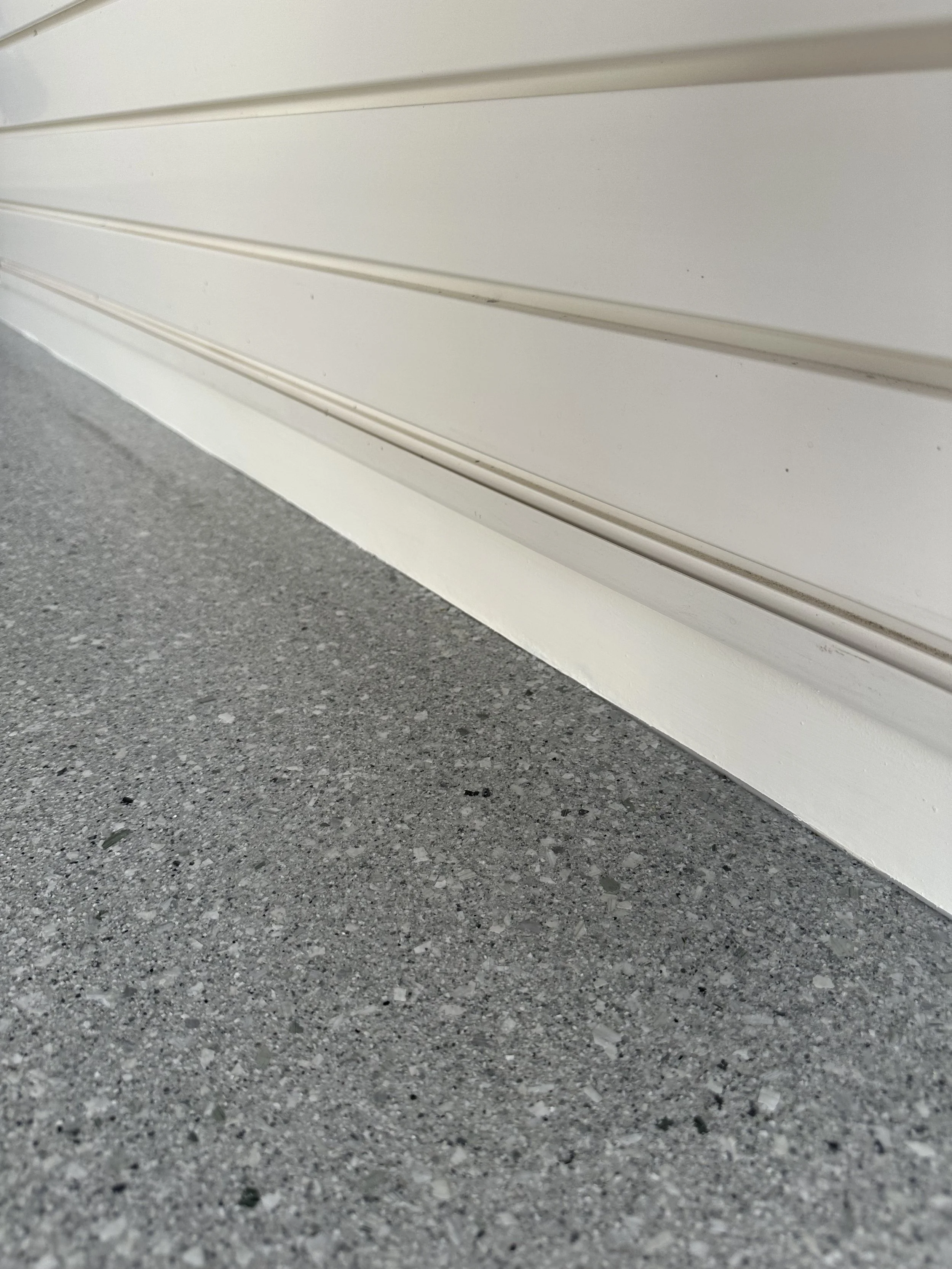 Close-up of a white garage door base and gray concrete driveway.