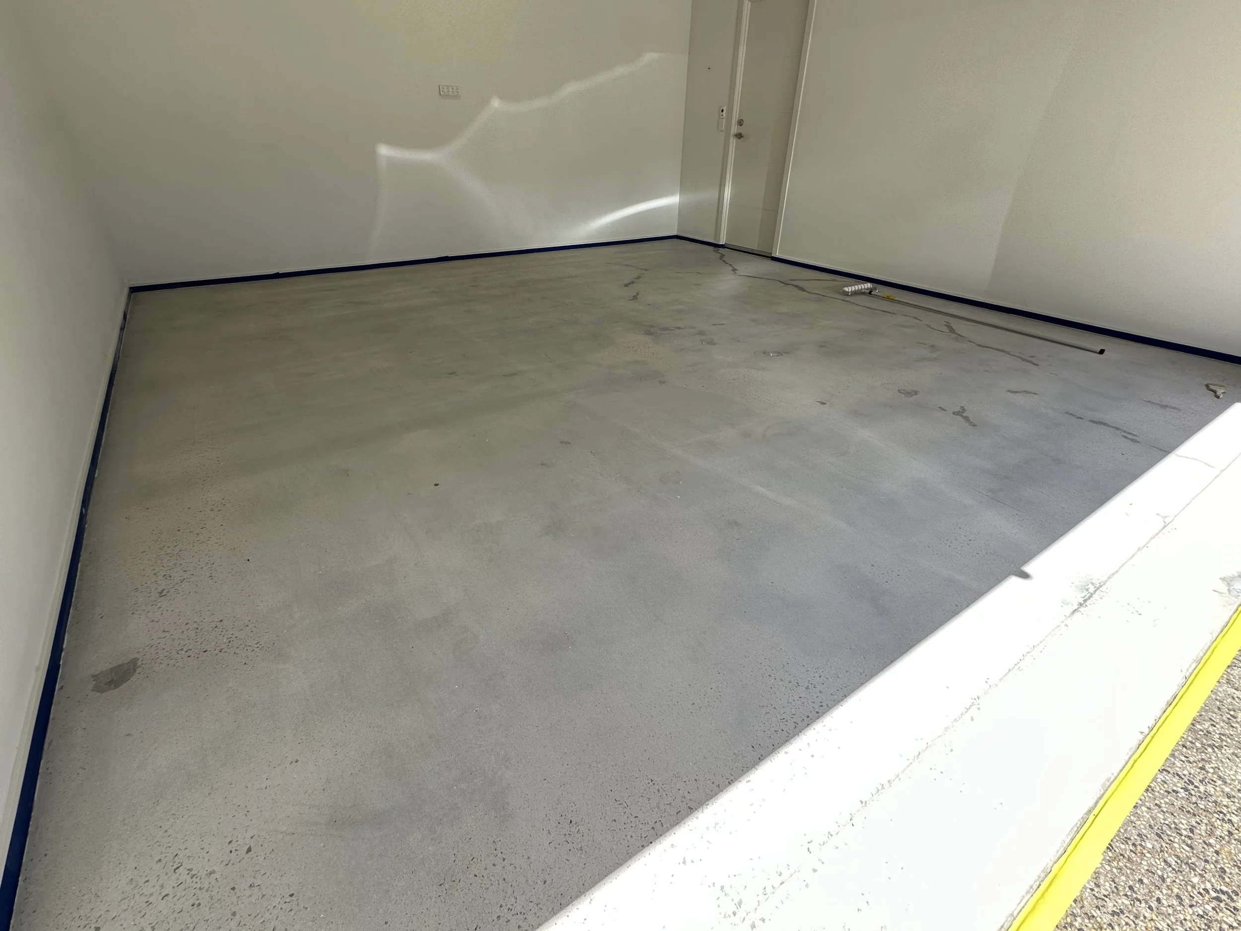 Empty garage with concrete floor, white walls, and a door in the background, with some construction tools on the floor.