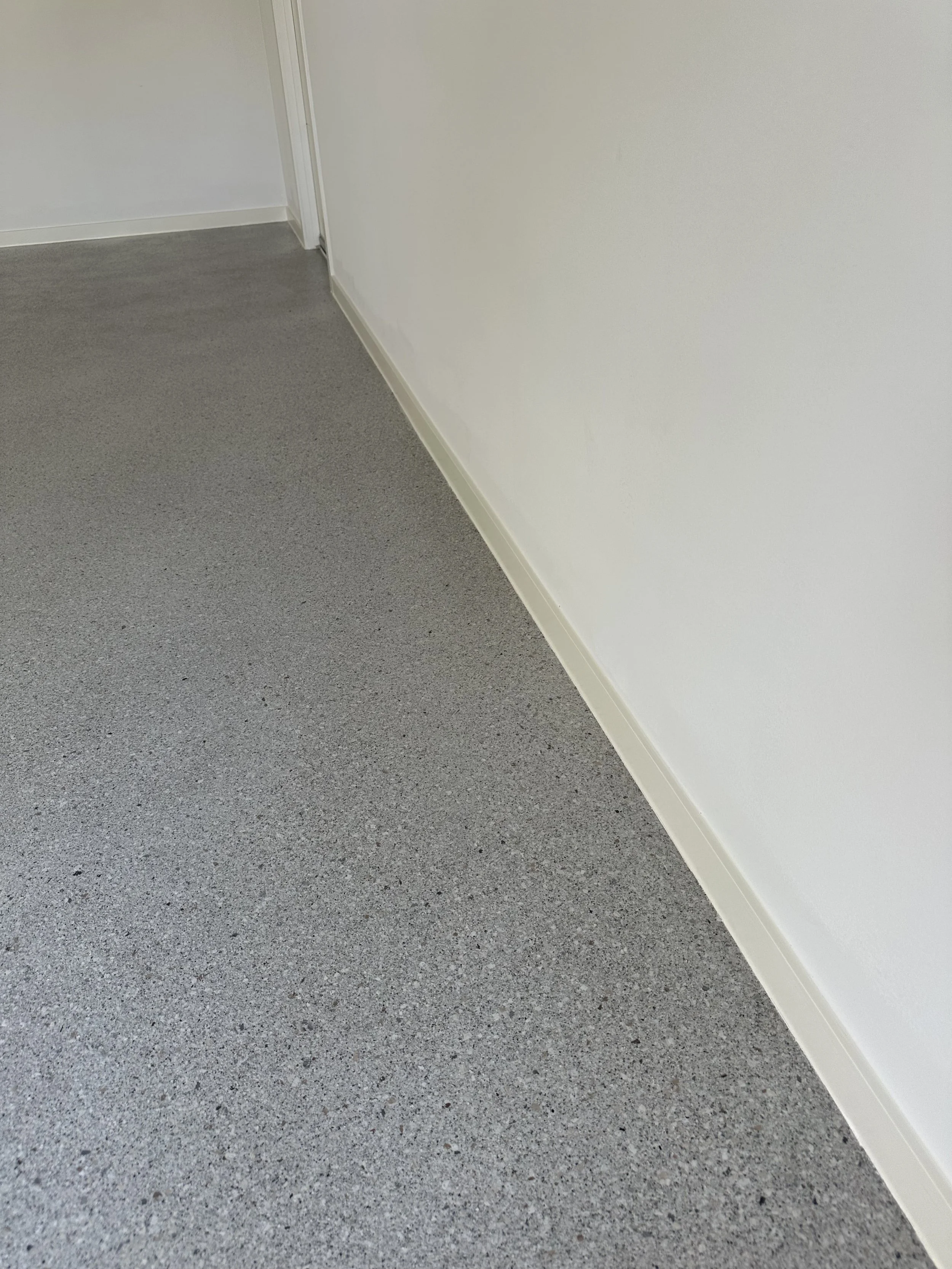 Close-up of a gray speckled floor with white baseboard along a wall and a partially visible door frame.