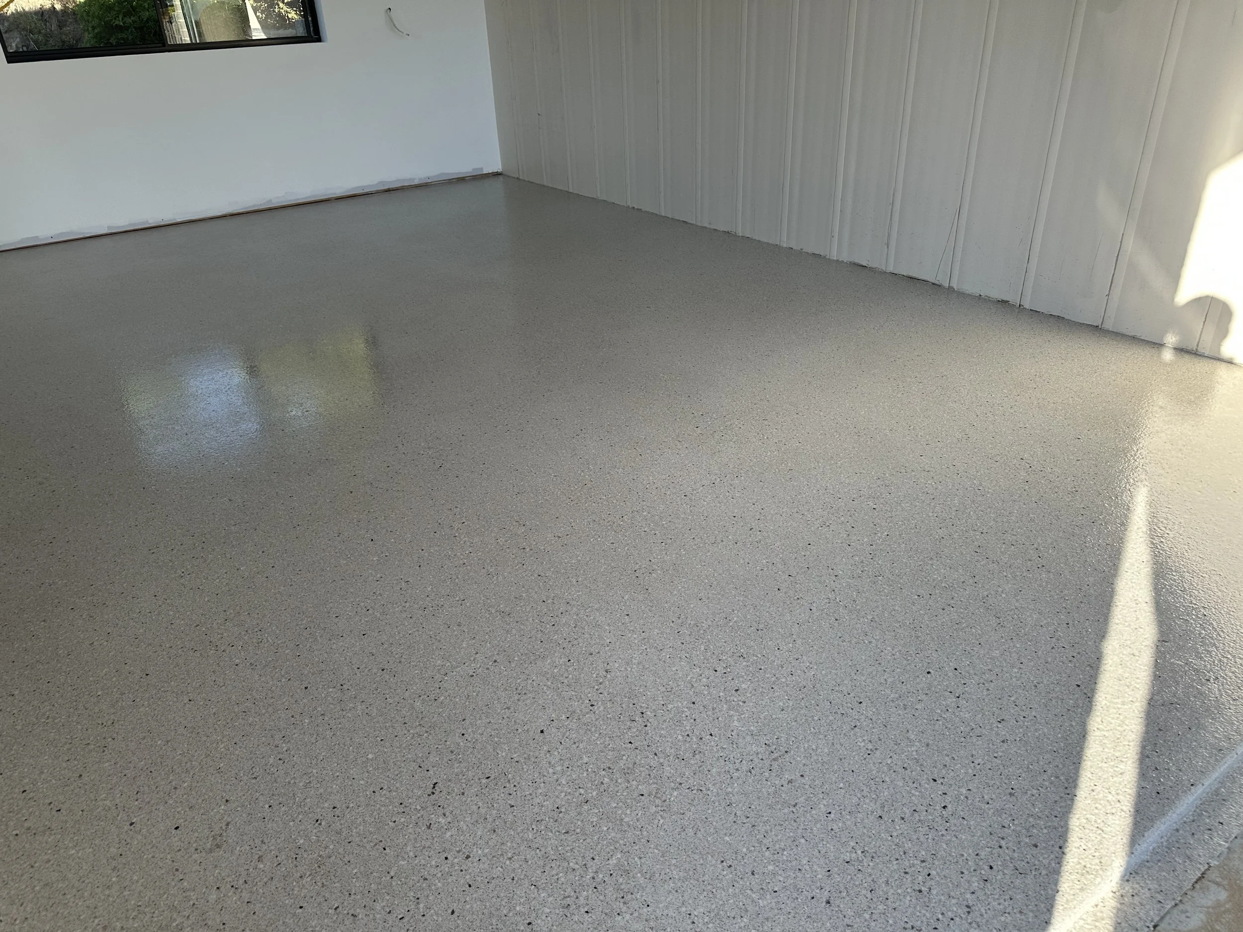 Empty room with polished concrete floor, white walls, and a window revealing outside greenery.