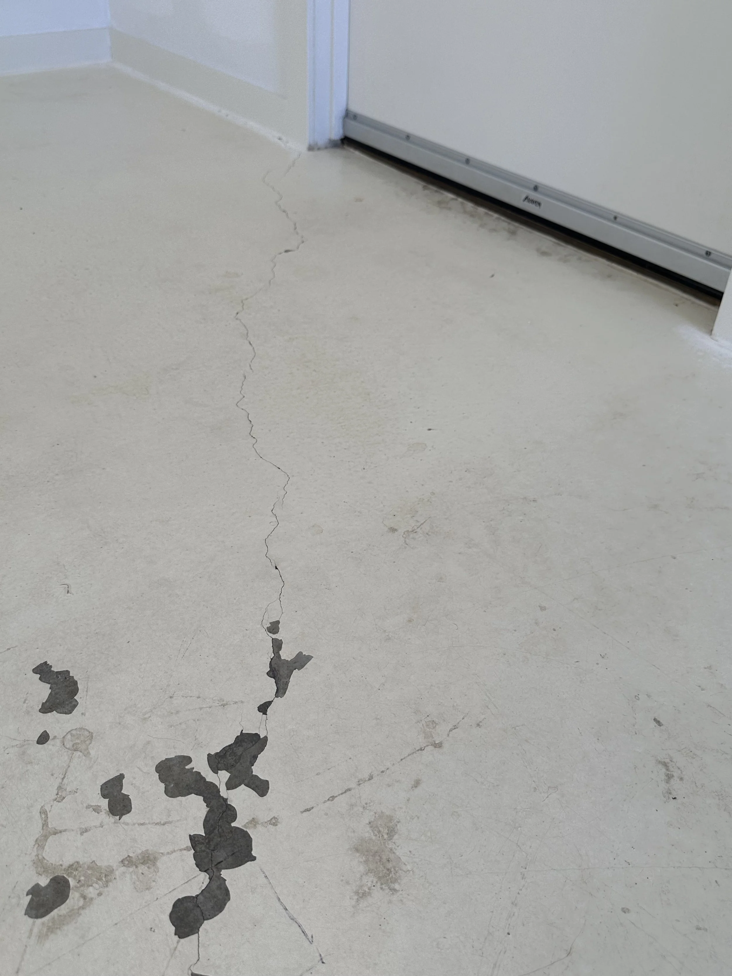 Crack in the concrete floor near a door with some water stains and debris.