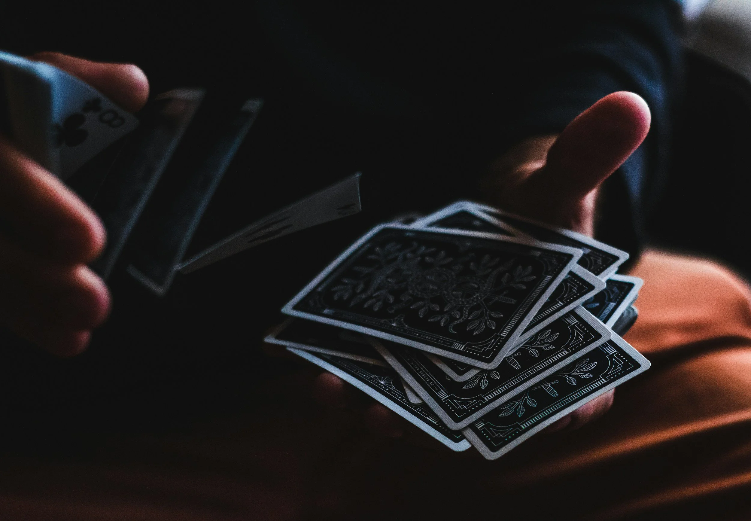 Close-up of a person holding a deck of black and white playing cards, fanned out in their hand, with a dark background.