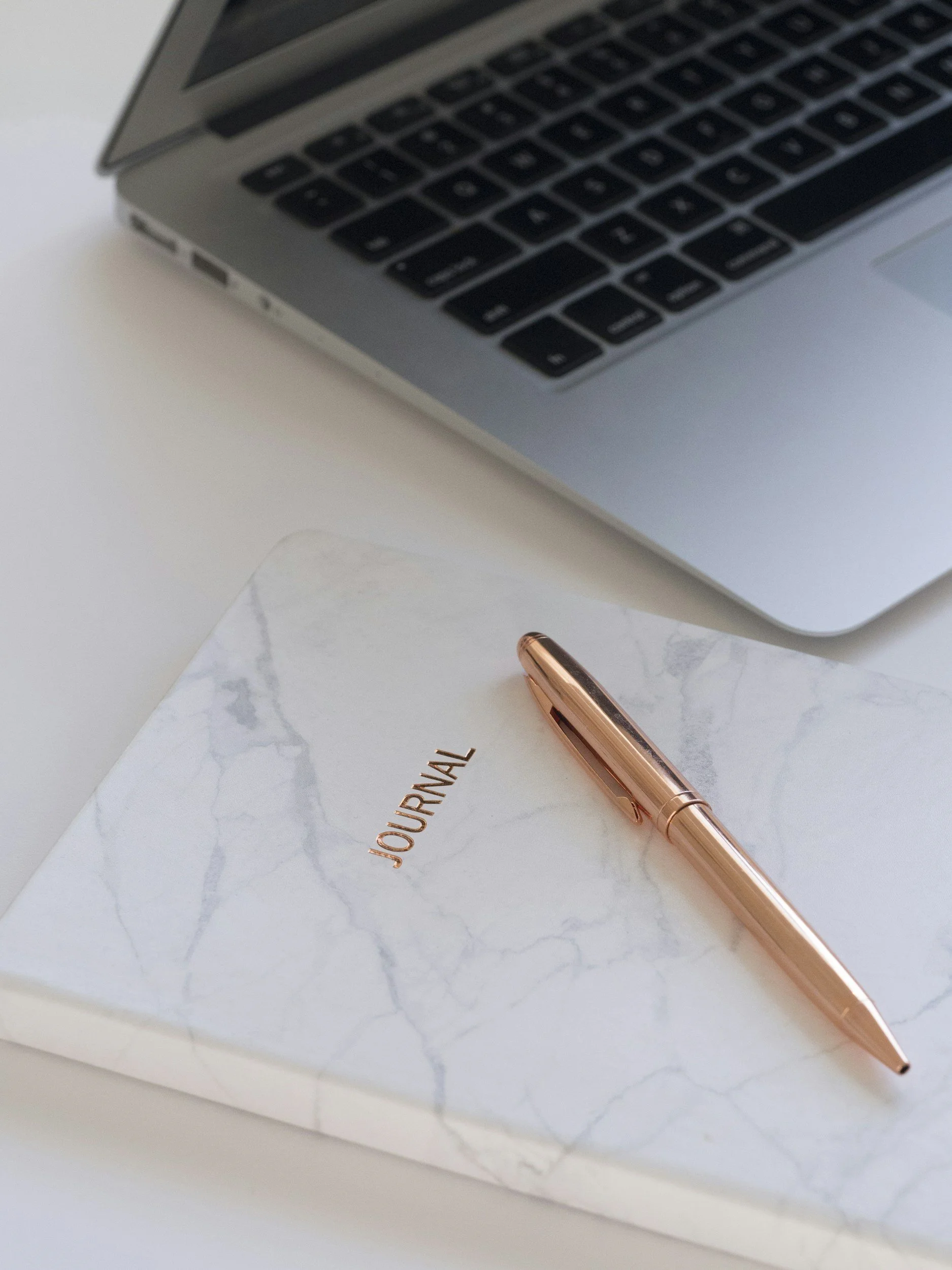 White journal notebook, gold pen, and laptop