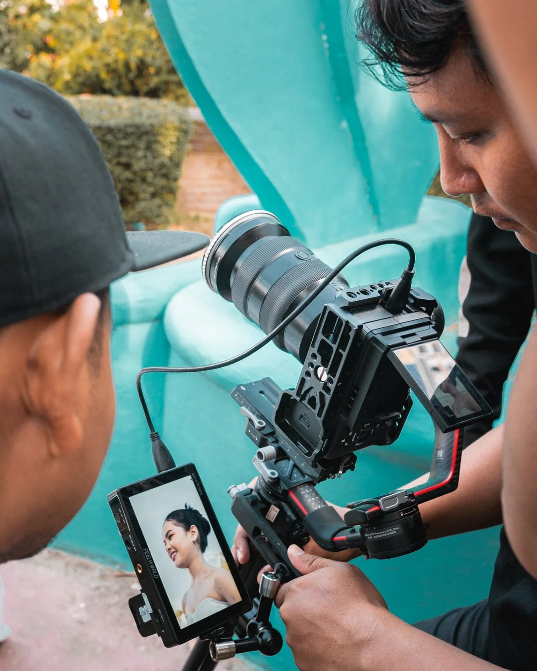 Twee fotografen film maken van een glimlachende vrouw in een witte jurk tijdens een fotoshoot buiten.