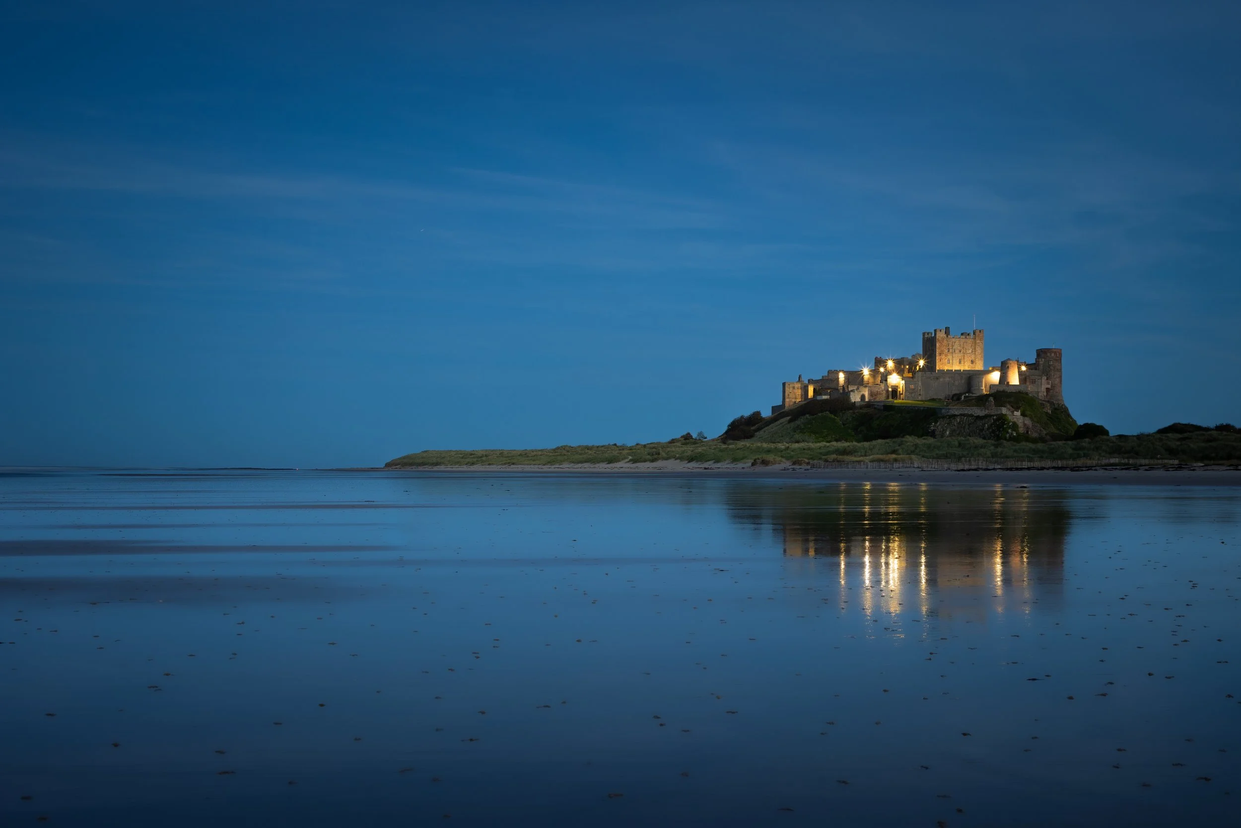 Bamburgh Castle during blue hour, reflecting in the wet sand