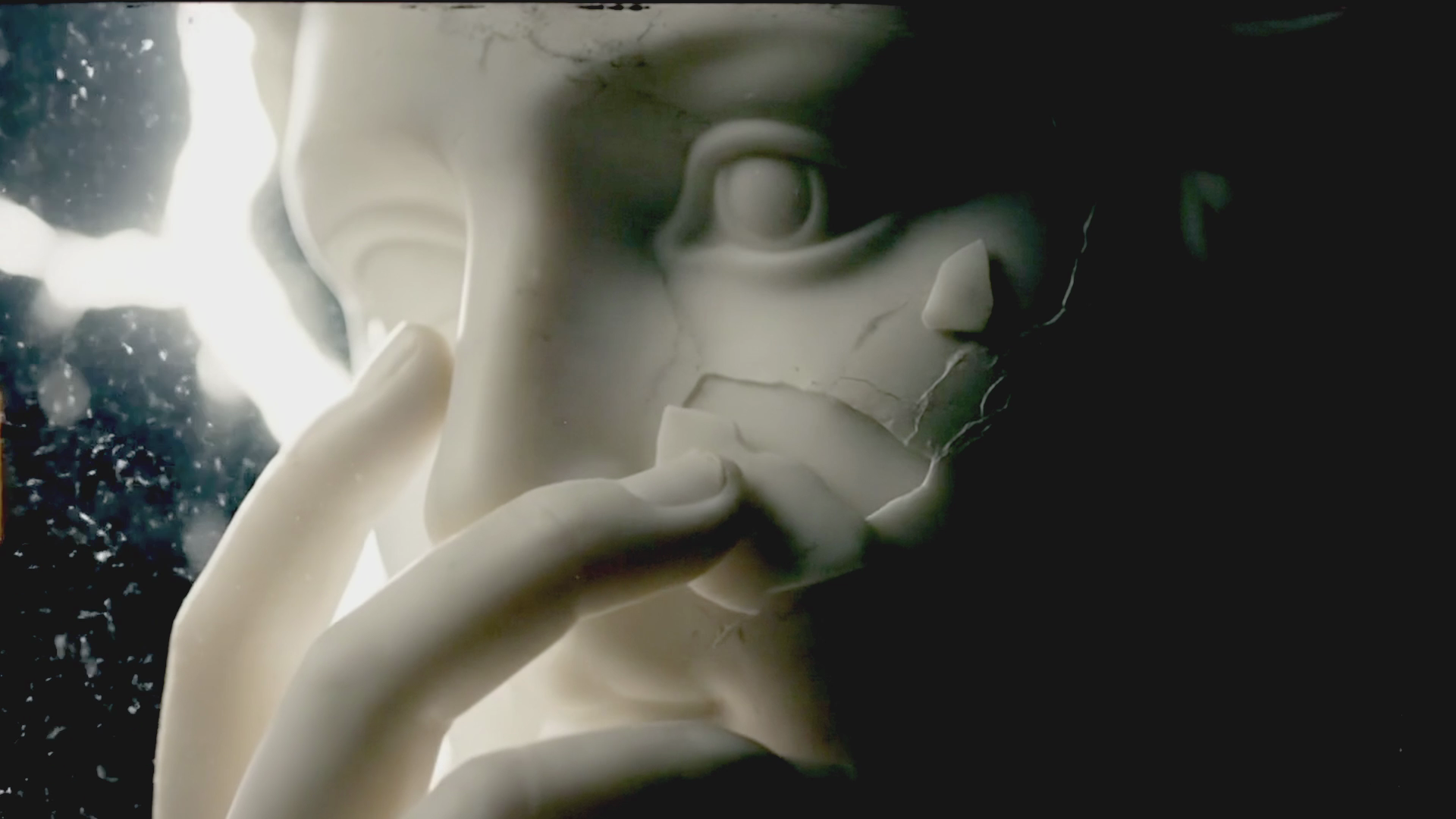 Close-up of a broken white marble statue of a person's face with a finger touching the lips, with a dark background and light shining from the left.