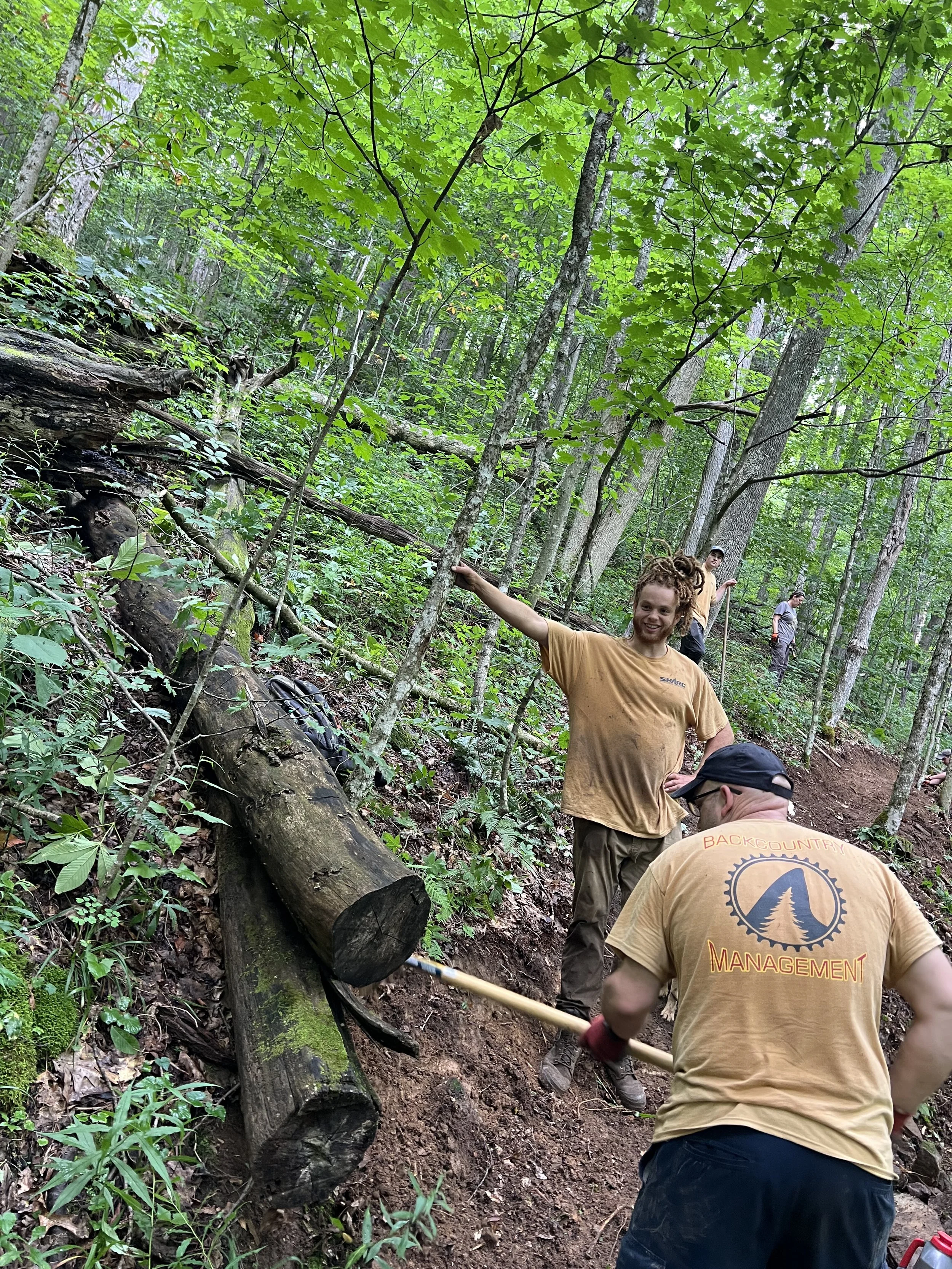 A group of trail crew workers on trail, one is leaning on a tree