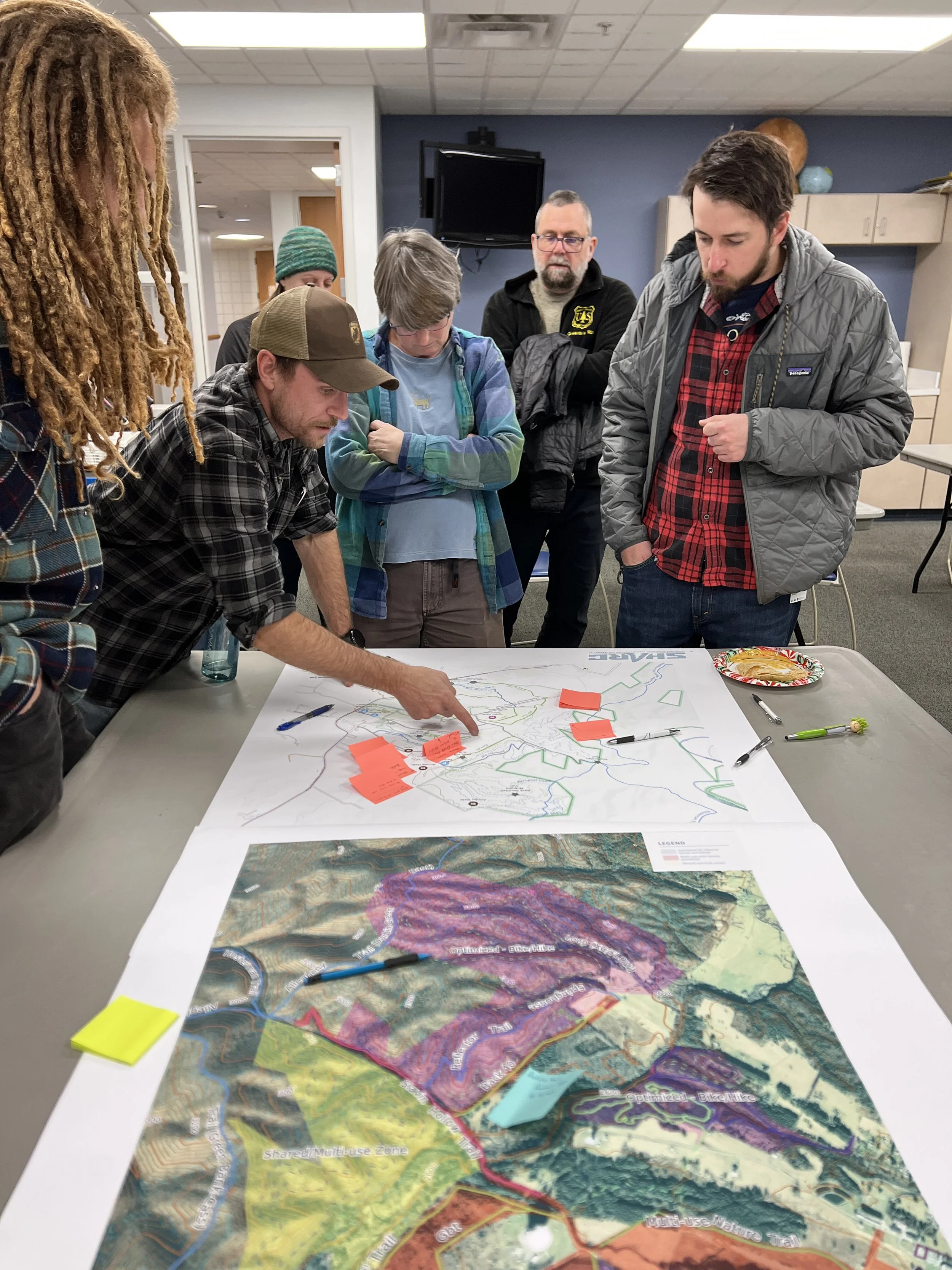 A group of people gathered around a table with maps, discussing planning or community development.