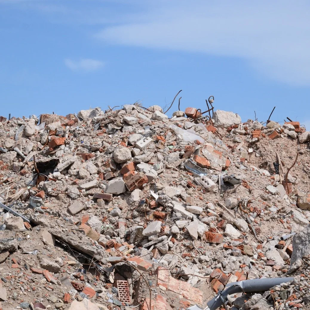 Pile of rubble and debris with broken bricks, metal, and concrete under a blue sky.