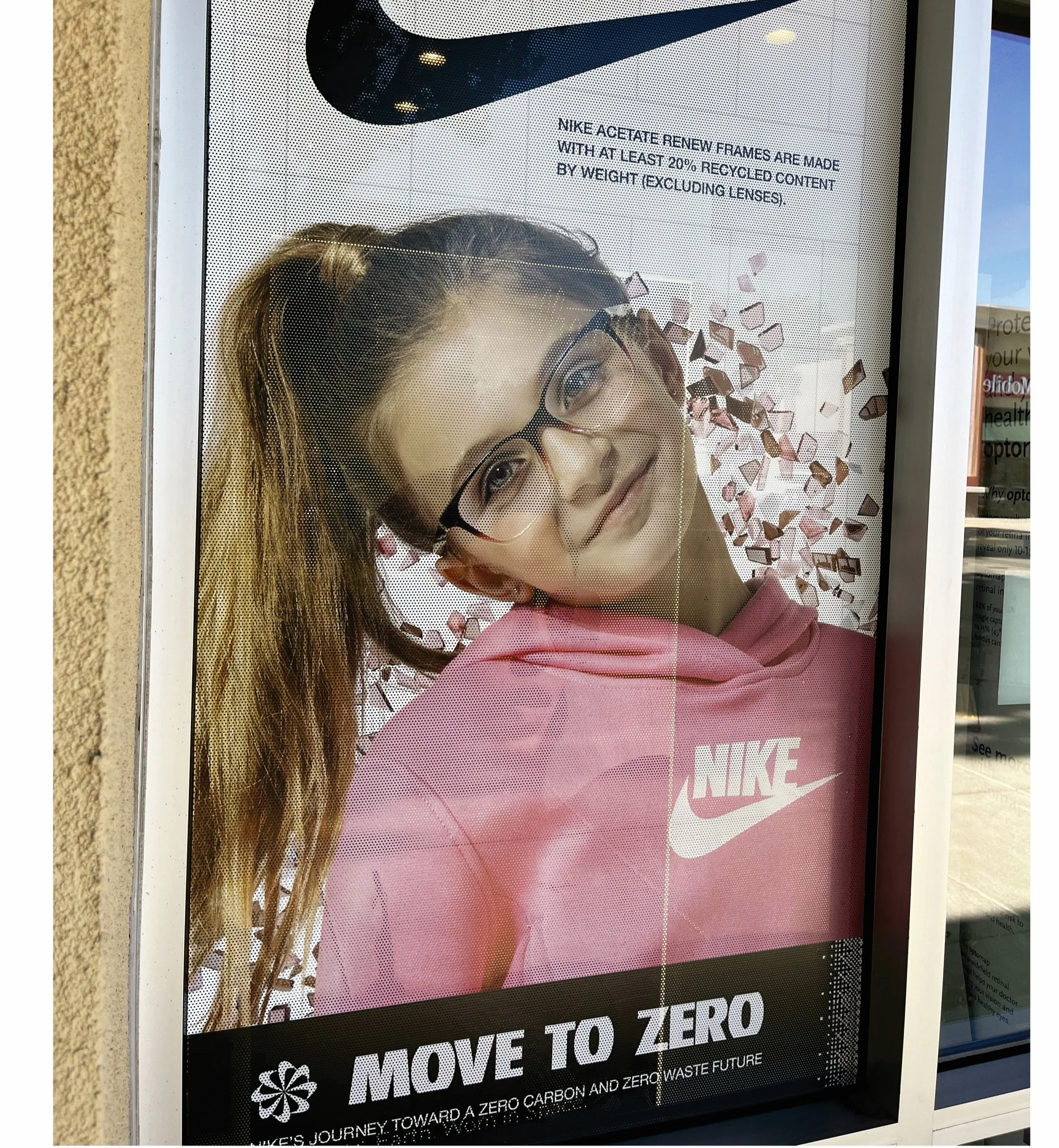 Advertisement featuring a young woman with glasses and wavy hair wearing a pink Nike hoodie, smiling and lying down with scattered pink and brown pieces around her. Text promotes Nike's eco-friendly initiatives and zero waste goals.